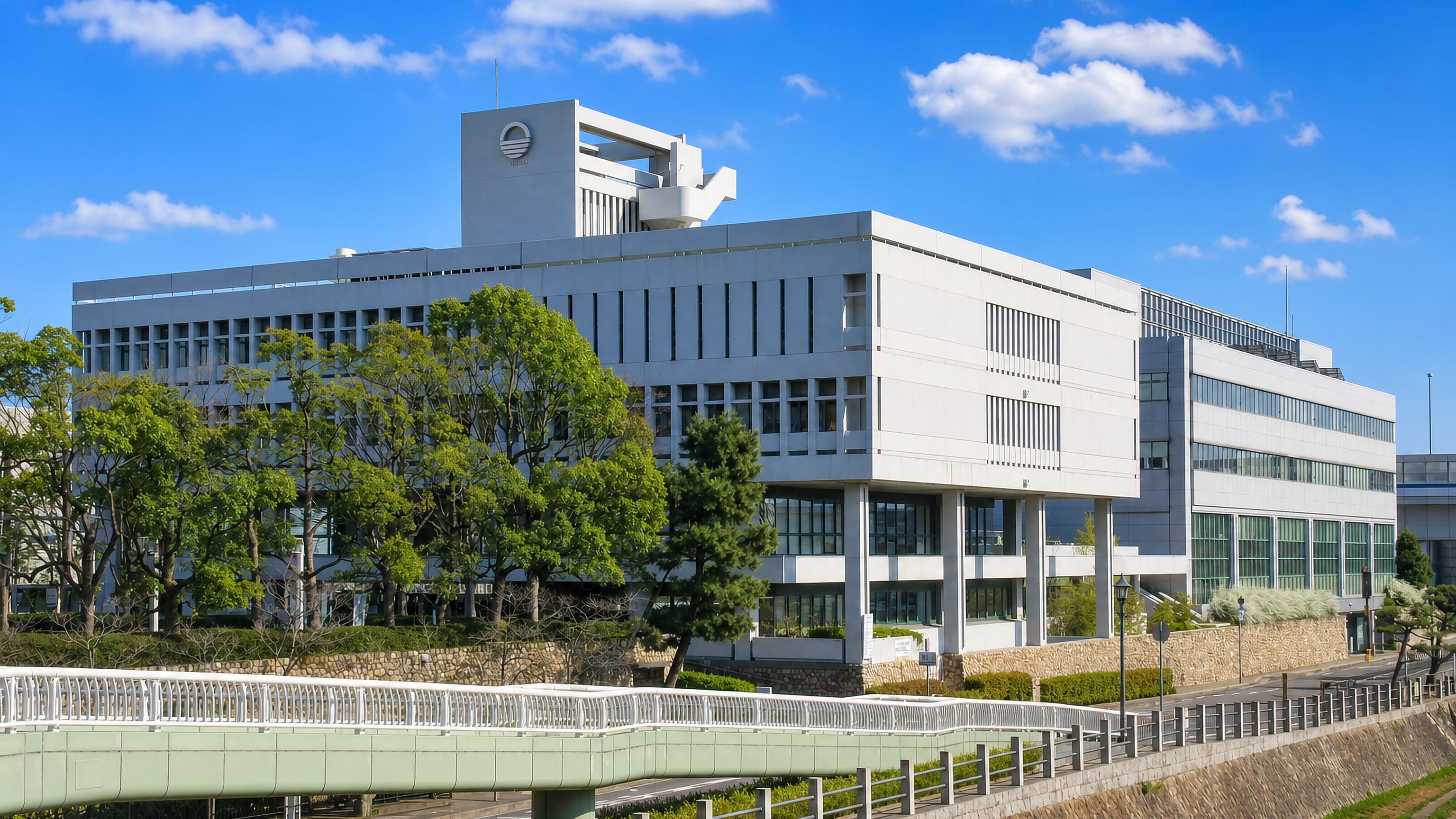 The white modernist civic building of Ashiya, Japan, above a footbridge and landscaped riverside terrace.