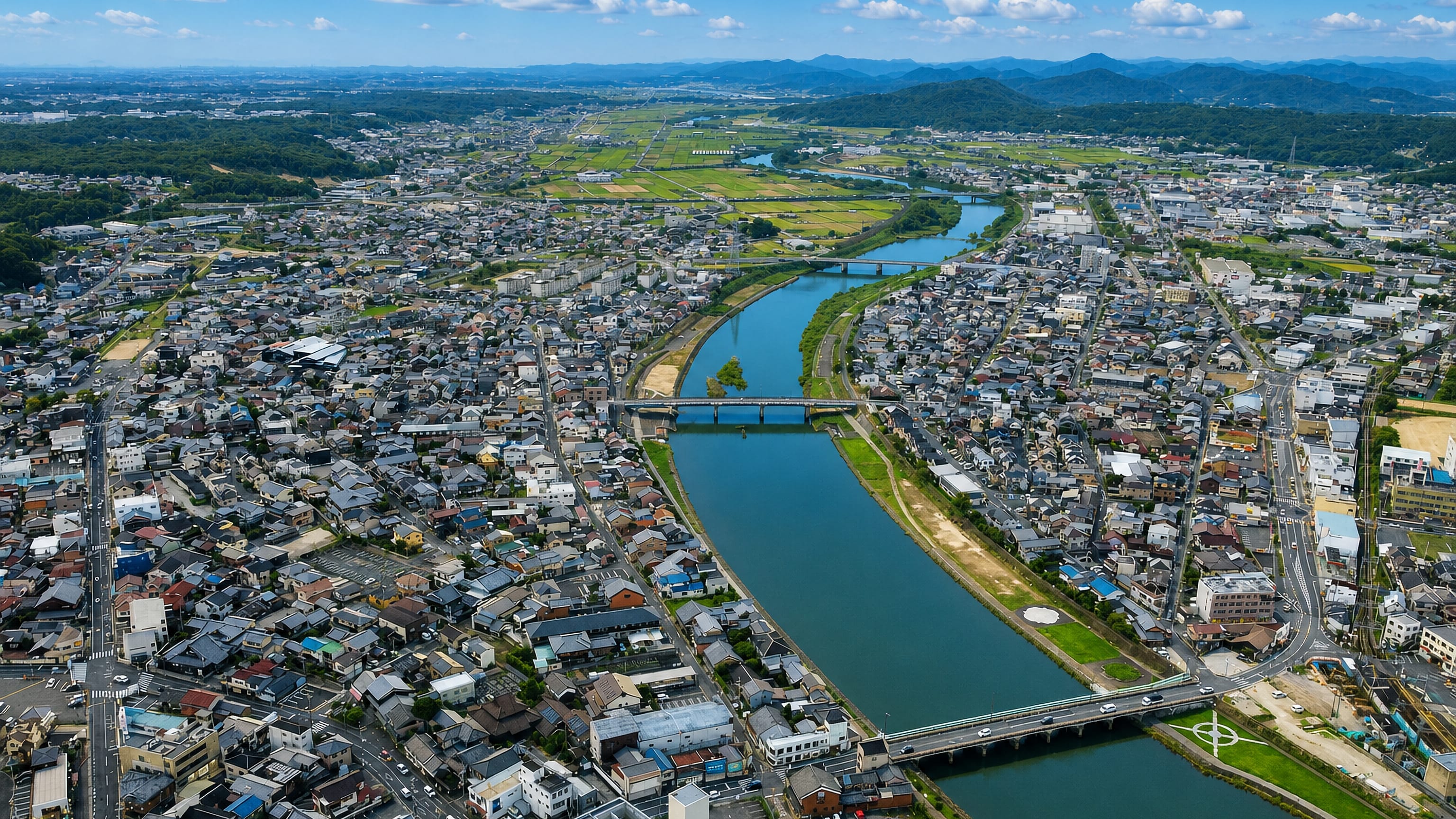 Aerial view of Miki, Hyōgo, spread along its river with road bridges and wooded hills beyond.