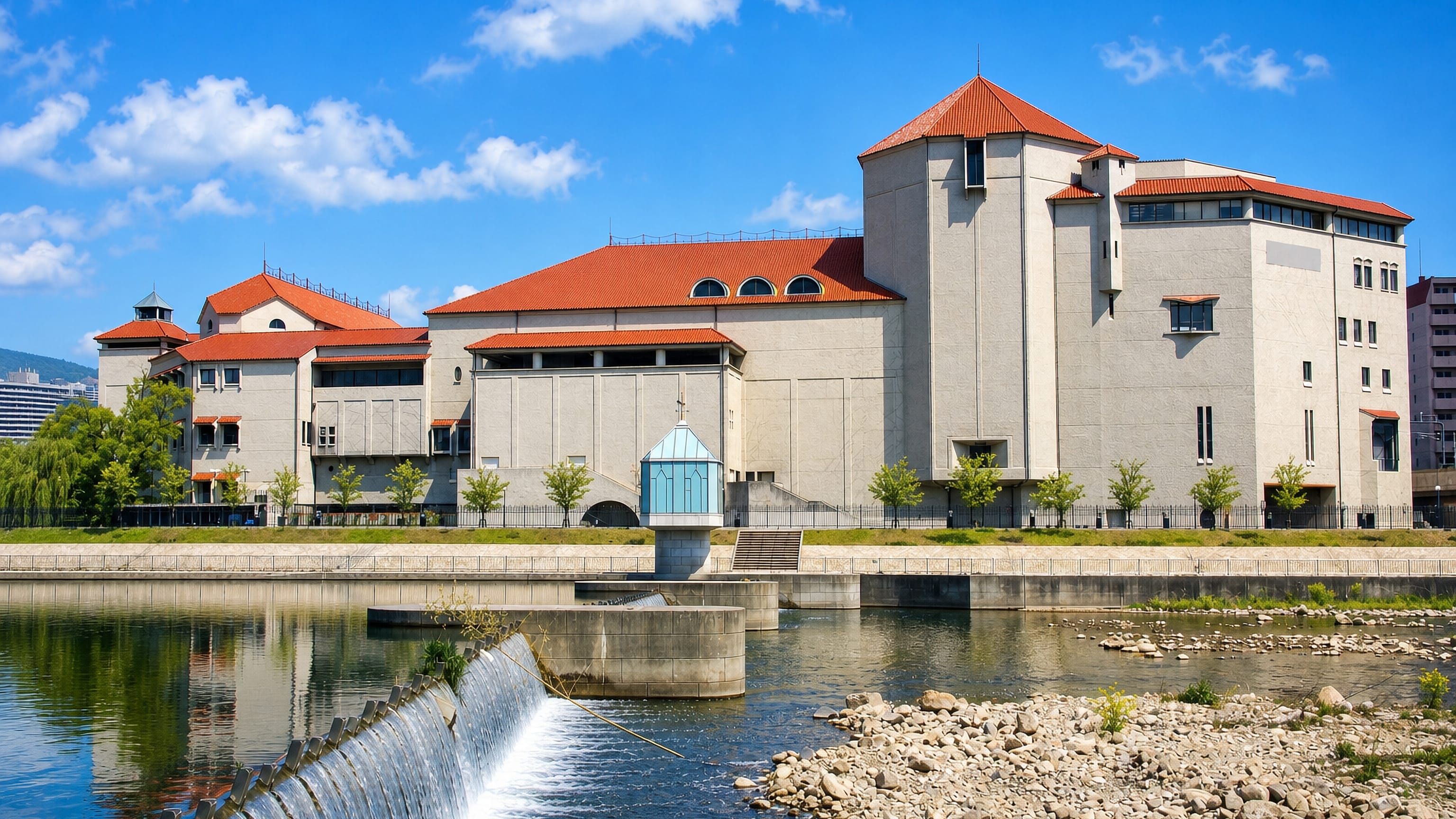The riverside Takarazuka Grand Theater and its red-tiled roofs above a weir on the Muko River, Takarazuka, Japan.