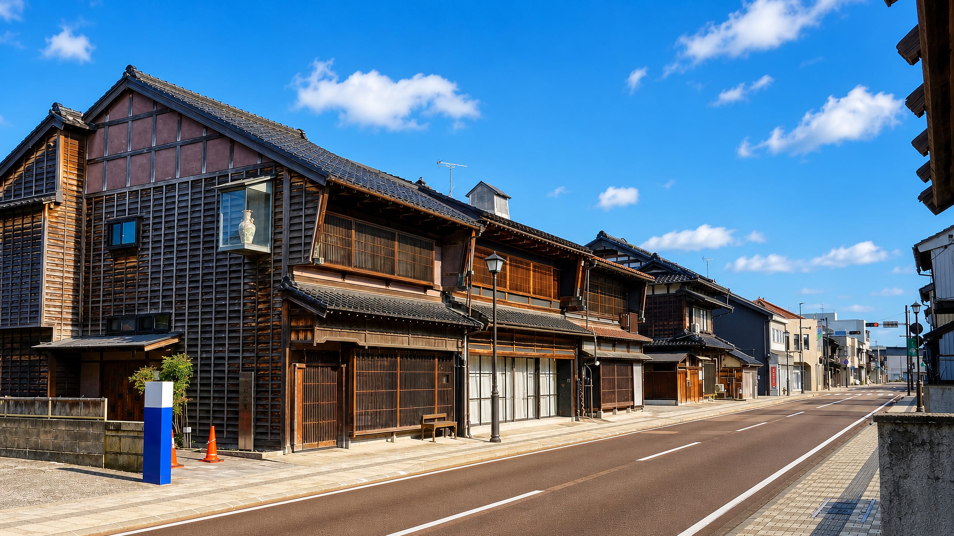 Preserved wooden merchant houses lining a quiet street in Komatsu, Ishikawa, under a bright blue sky.