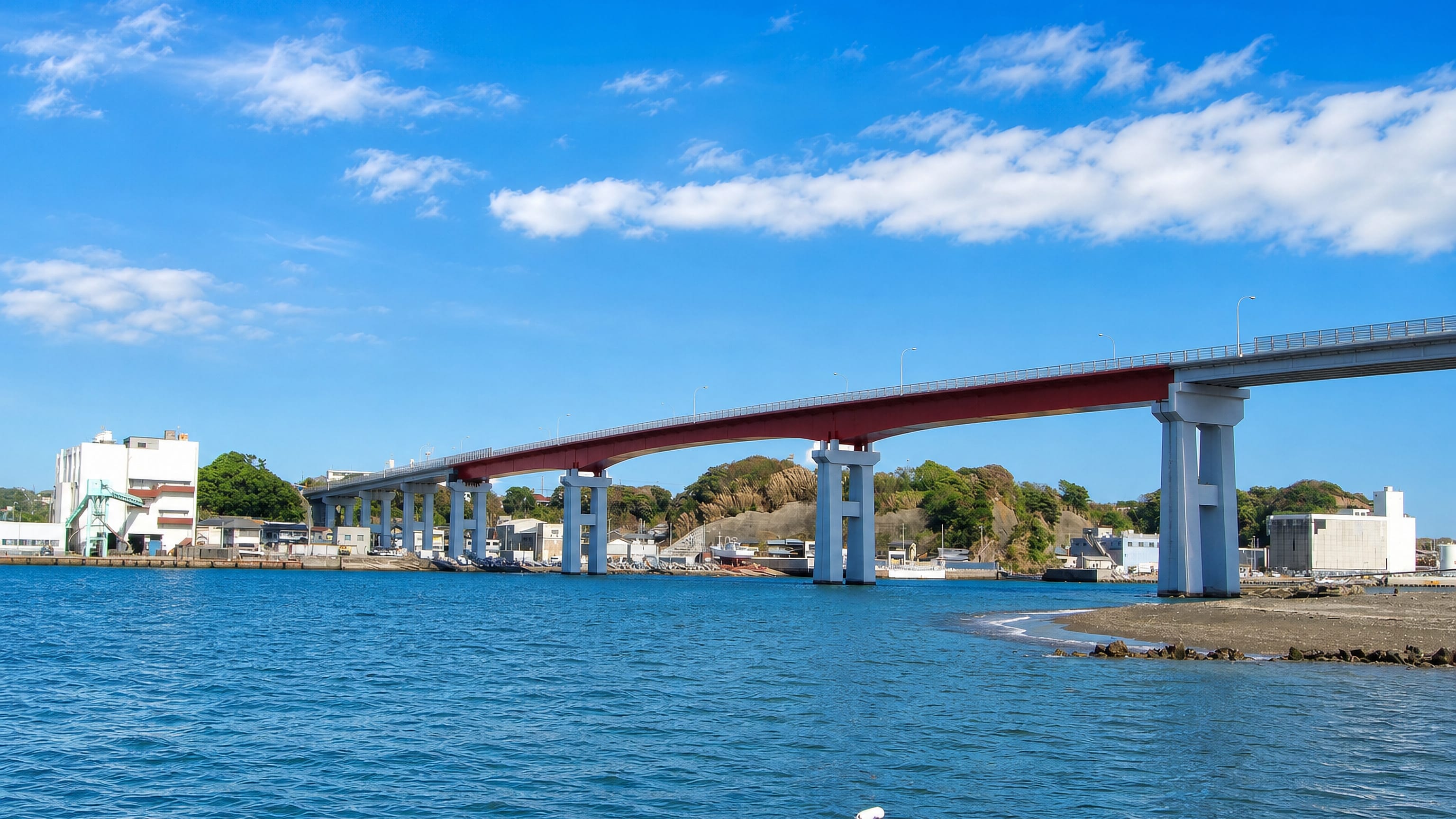 Red-girder road bridge spanning the harbour channel at Miura, Japan, with the port town behind.