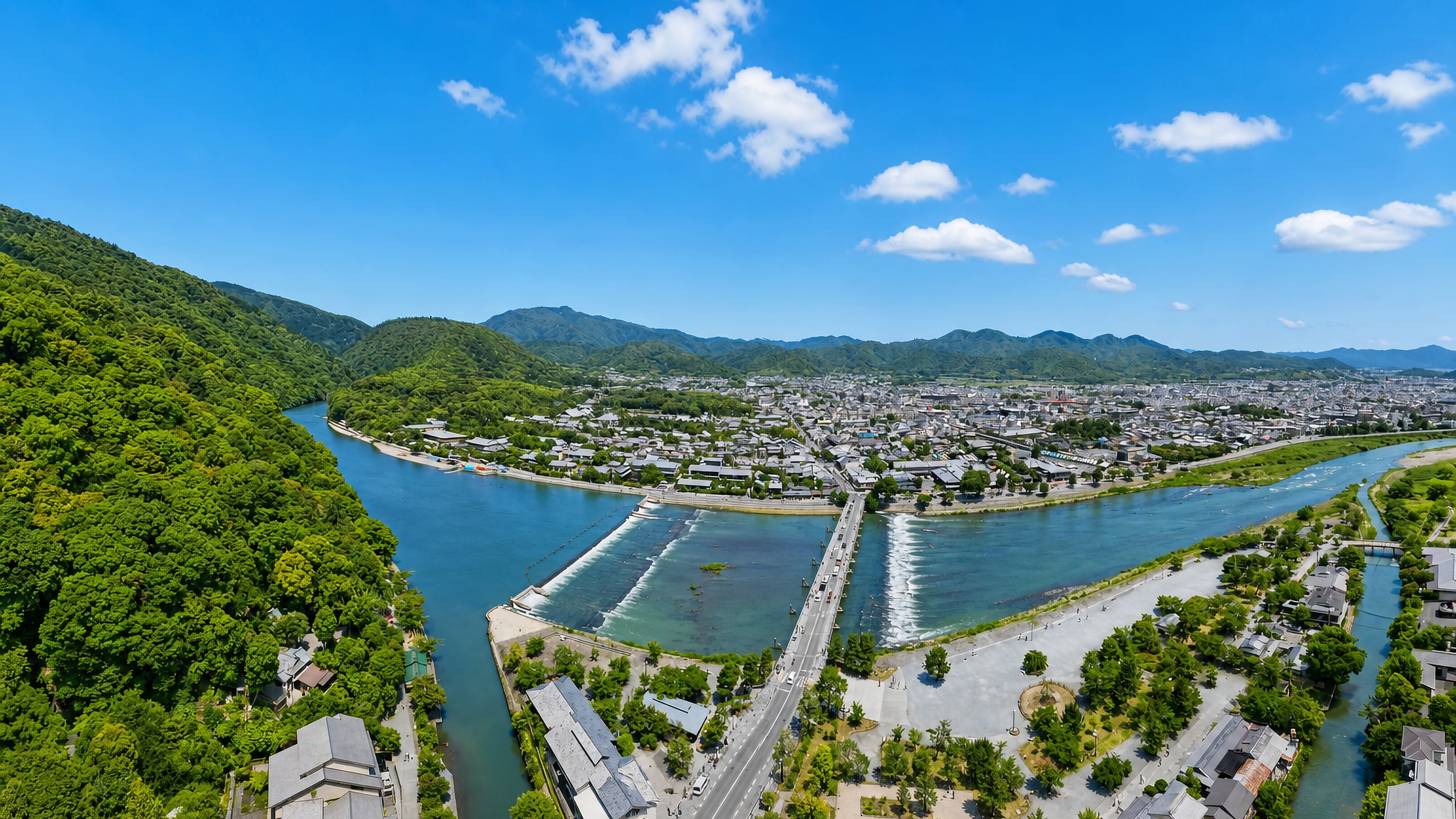 Aerial view of Arashiyama, Kyoto, with the Togetsukyo Bridge spanning the Katsura River below wooded hills.