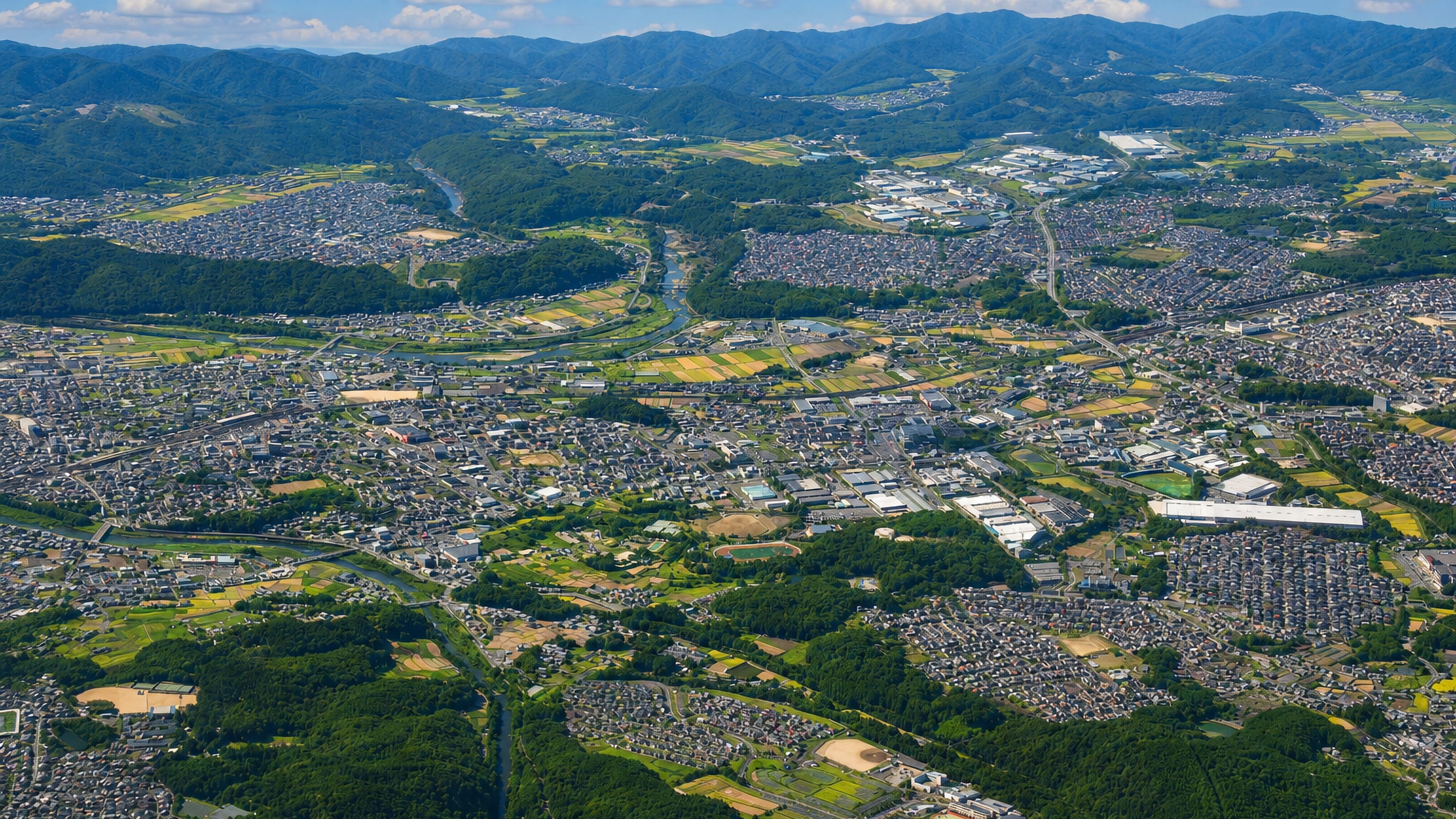 Aerial over Nabari's houses, rice paddies and river valley ringed by the wooded hills of Mie