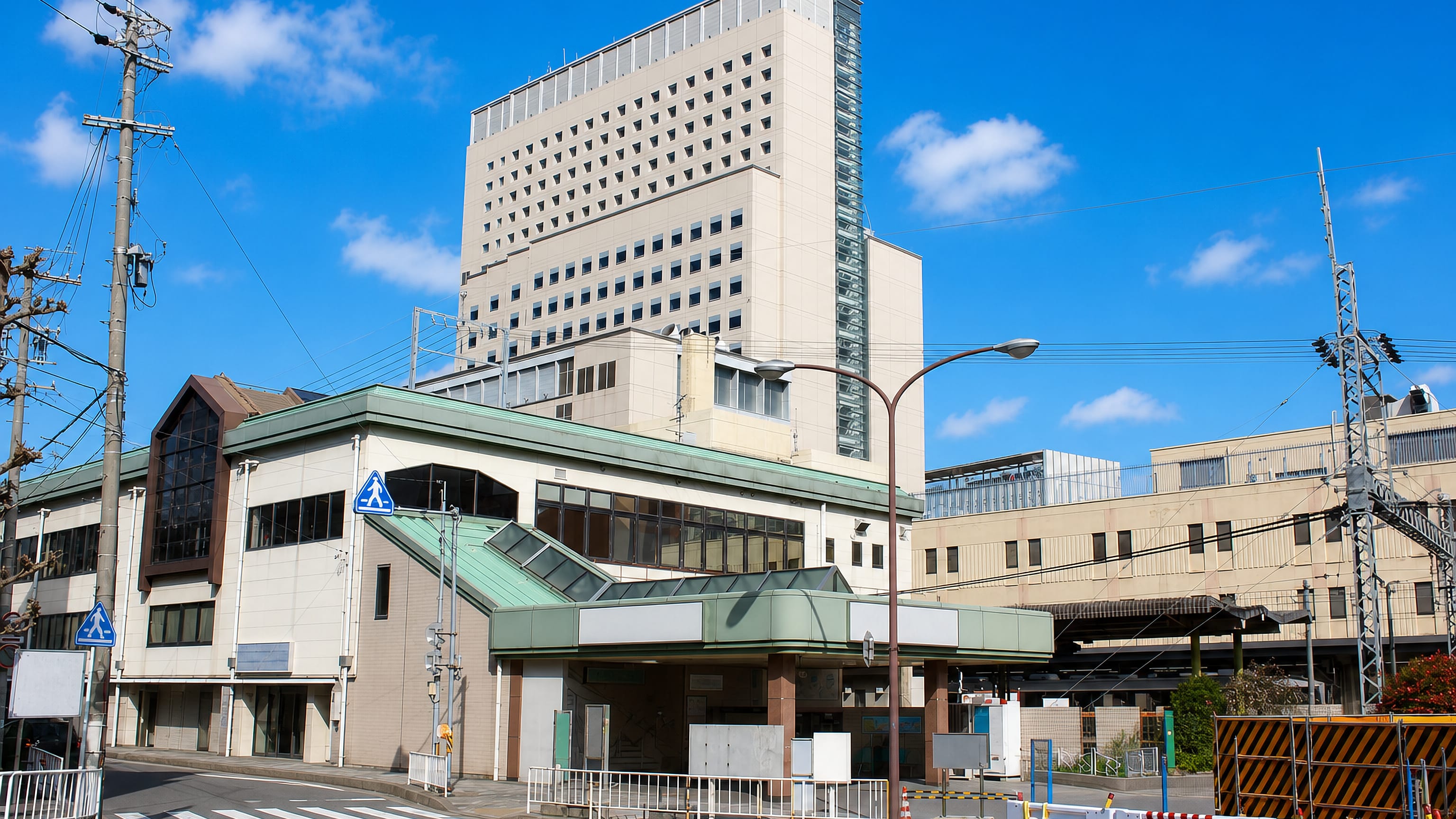 Station entrance and tall beige tower on a quiet street in Tsu, Mie Prefecture, under a clear sky