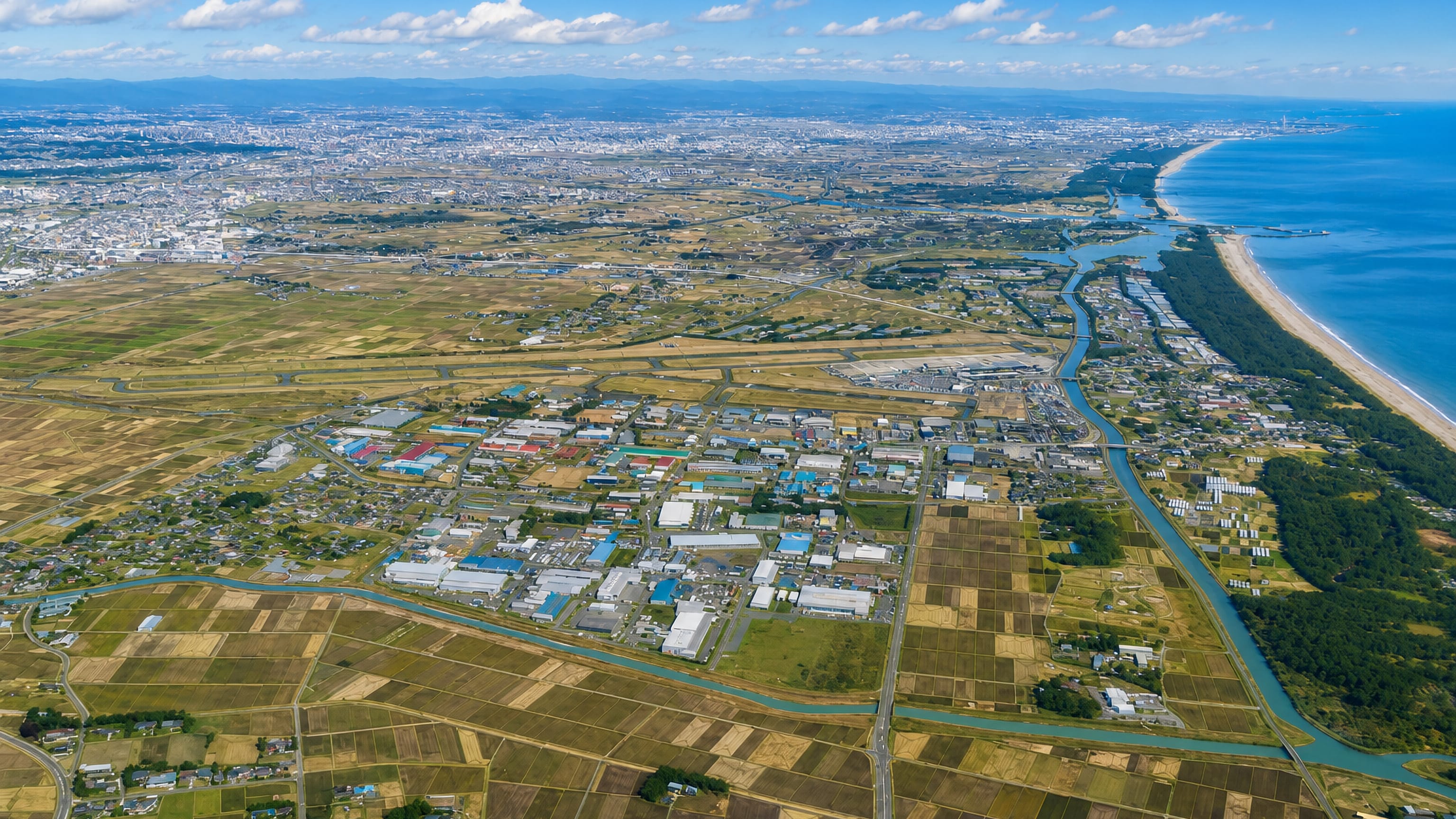 Aerial view of Natori, Japan, with rice paddies, an industrial park and canals meeting the Pacific coastline