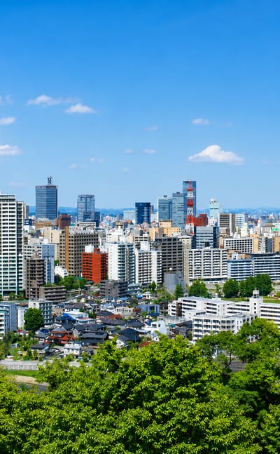 Sendai skyline in Miyagi, high-rise towers rising beyond the green trees of the surrounding hills.