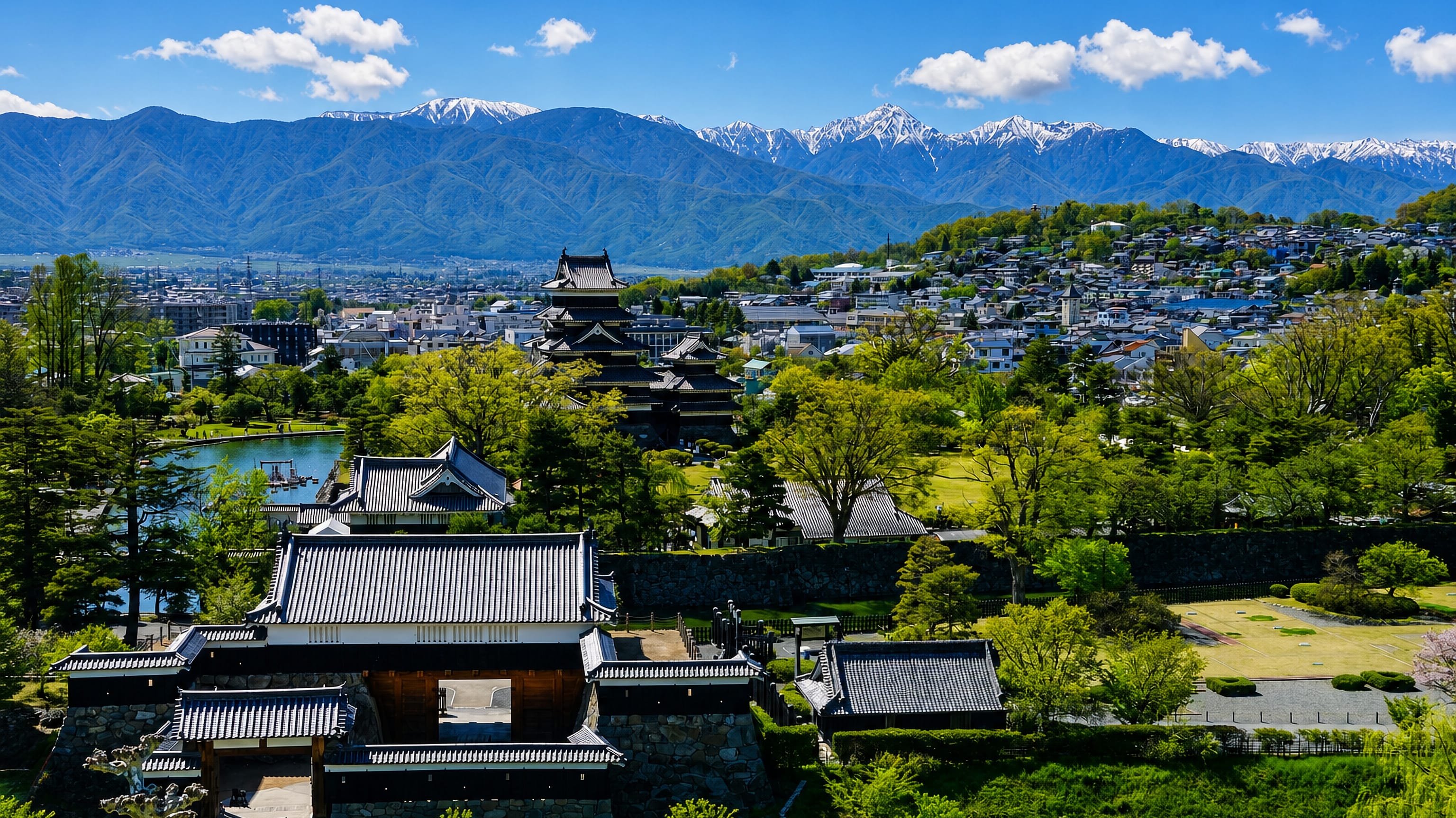 Matsumoto Castle's black keep and moat below the snow-capped Japanese Alps, with the city spreading beyond