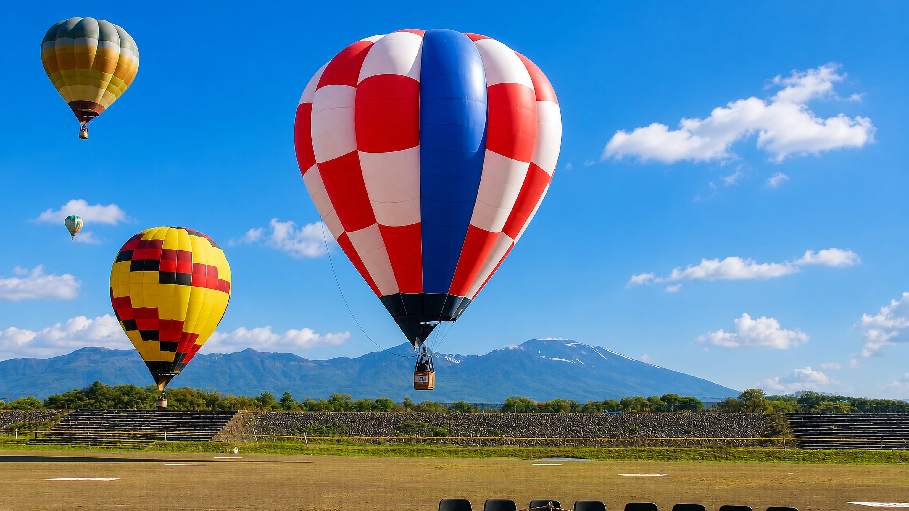 Hot-air balloons rising over a riverside field in Saku, Japan, with snow-streaked Mount Asama behind.