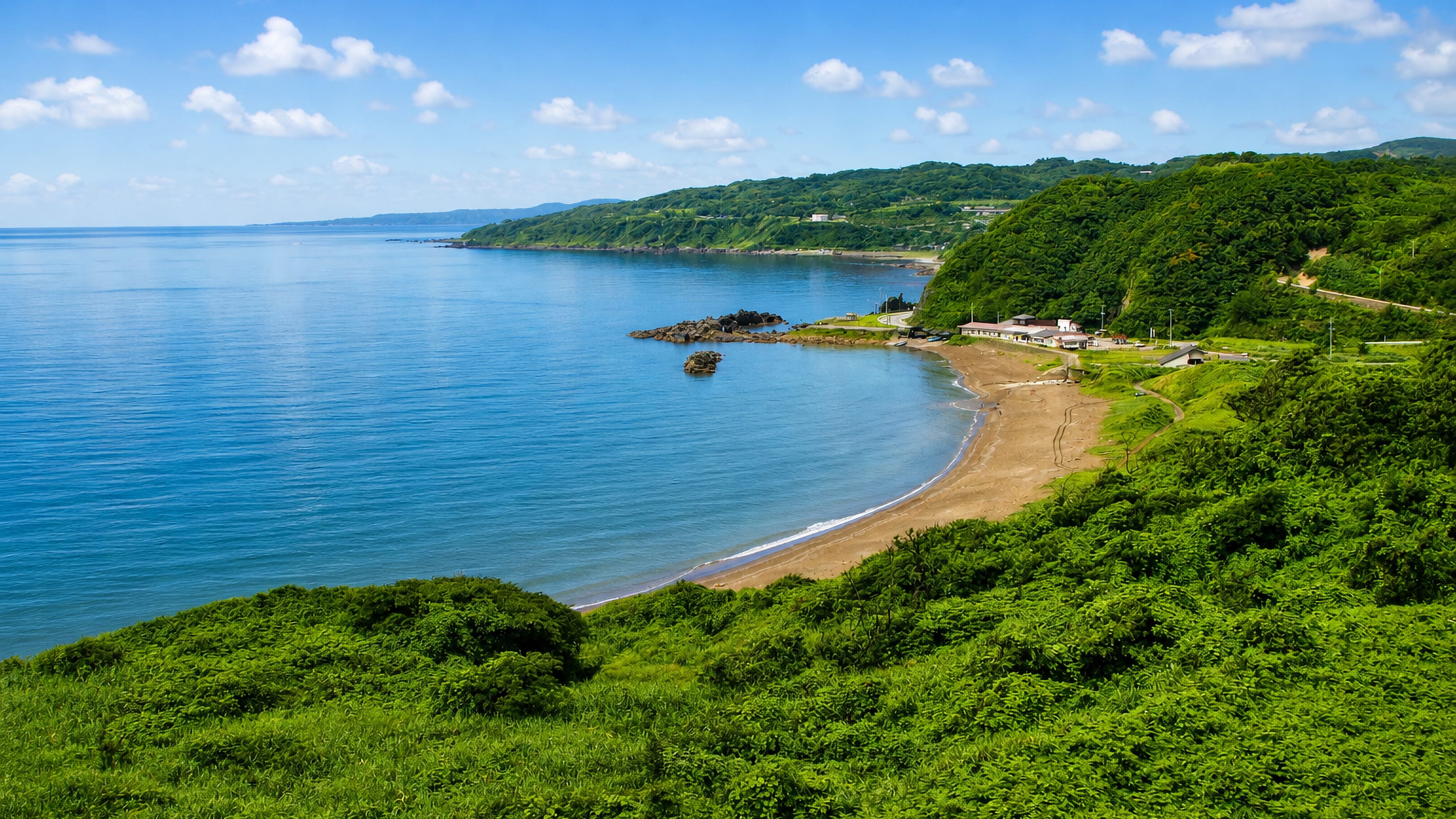 Green coastal hills above a curved sandy bay on Sado Island, Niigata, Japan.