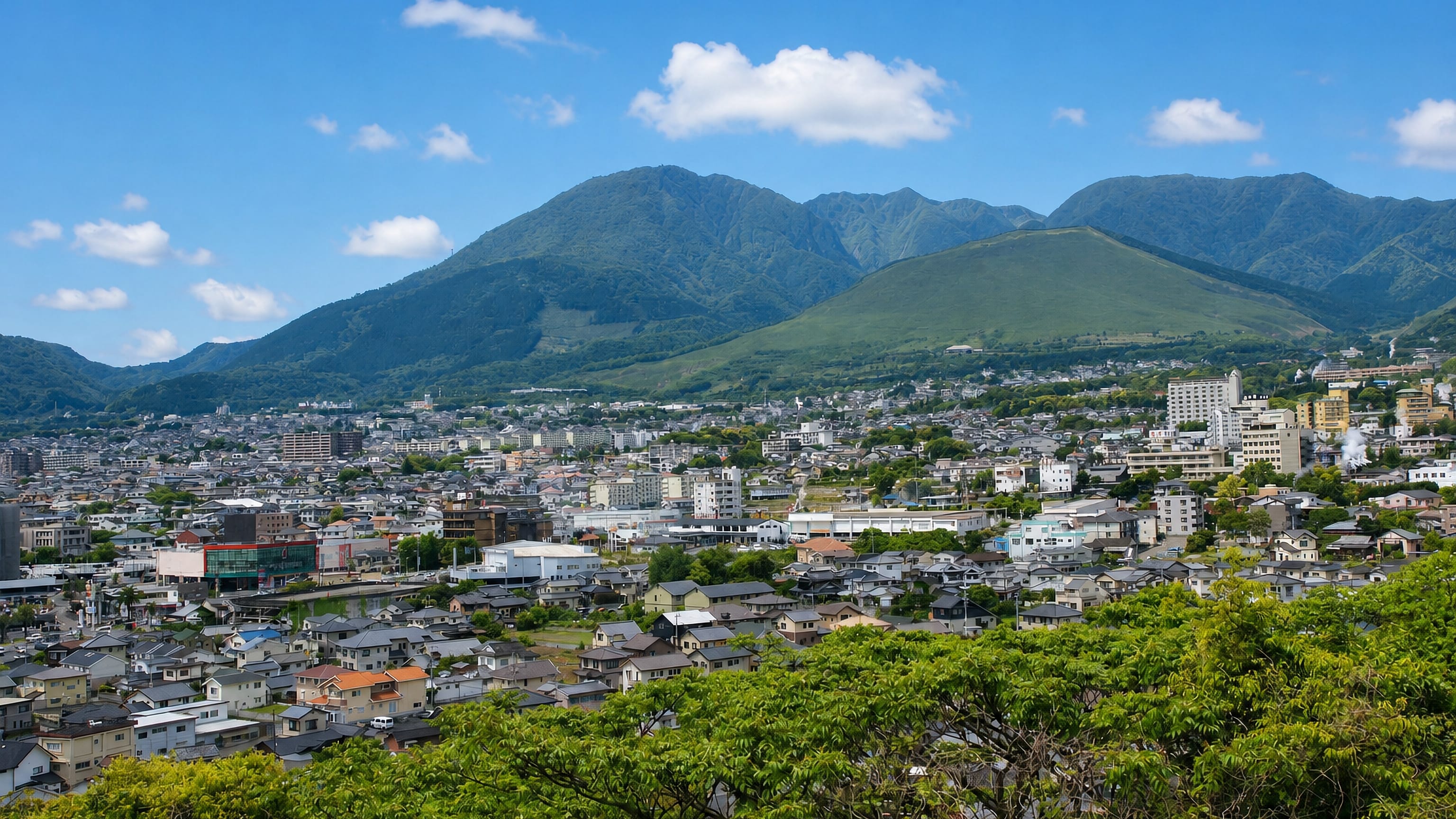 Hillside view over Beppu, Japan, with onsen steam rising above the town and the Tsurumi mountains behind.