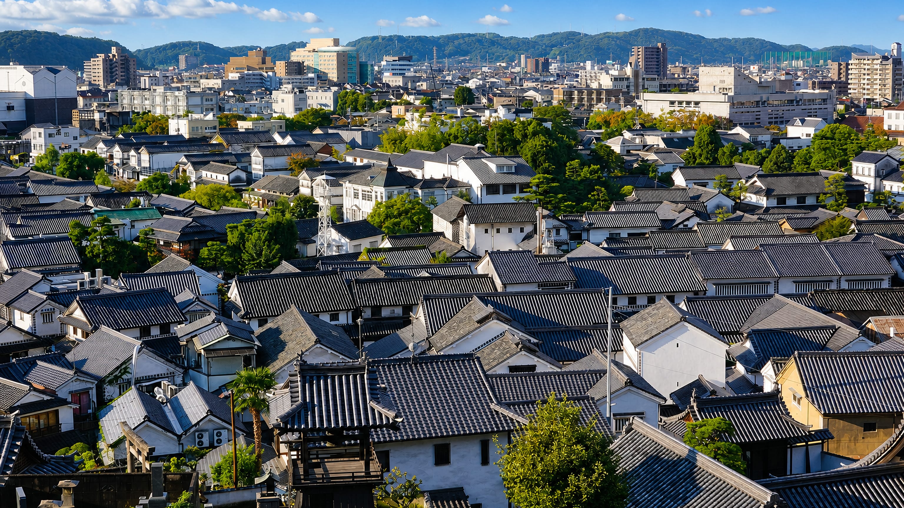 Tiled roofs and white-walled storehouses of Kurashiki's Bikan historical quarter, with hills on the horizon.