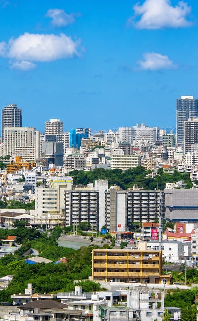 Naha cityscape in Okinawa, with dense mid-rise buildings and distant towers stretching toward the sea.