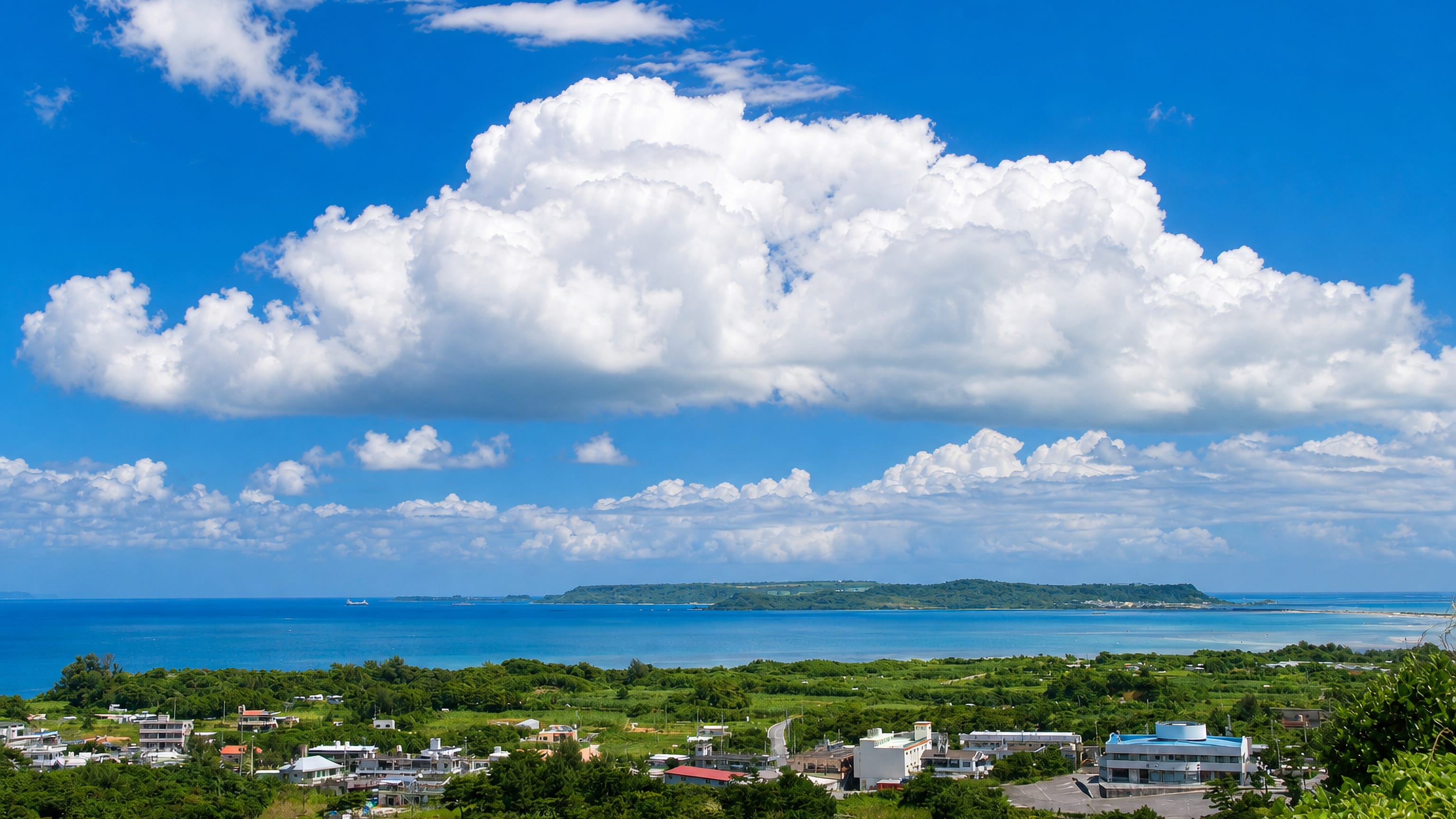 Coastal town of Uruma on Okinawa, with turquoise sea, offshore islands and towering summer clouds