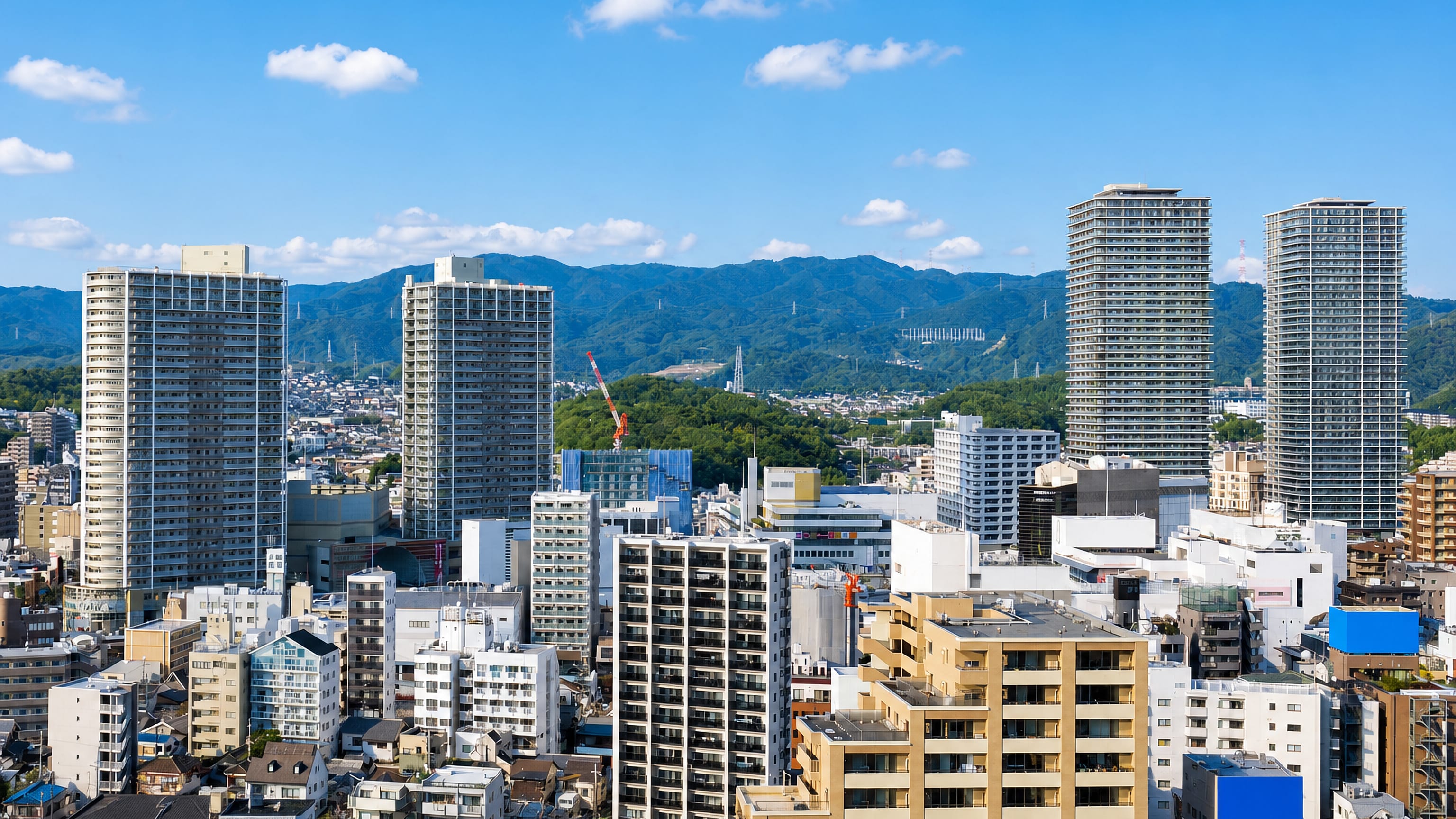 High-rise apartment towers above the low-rise centre of Takatsuki, Osaka, with wooded hills on the horizon.