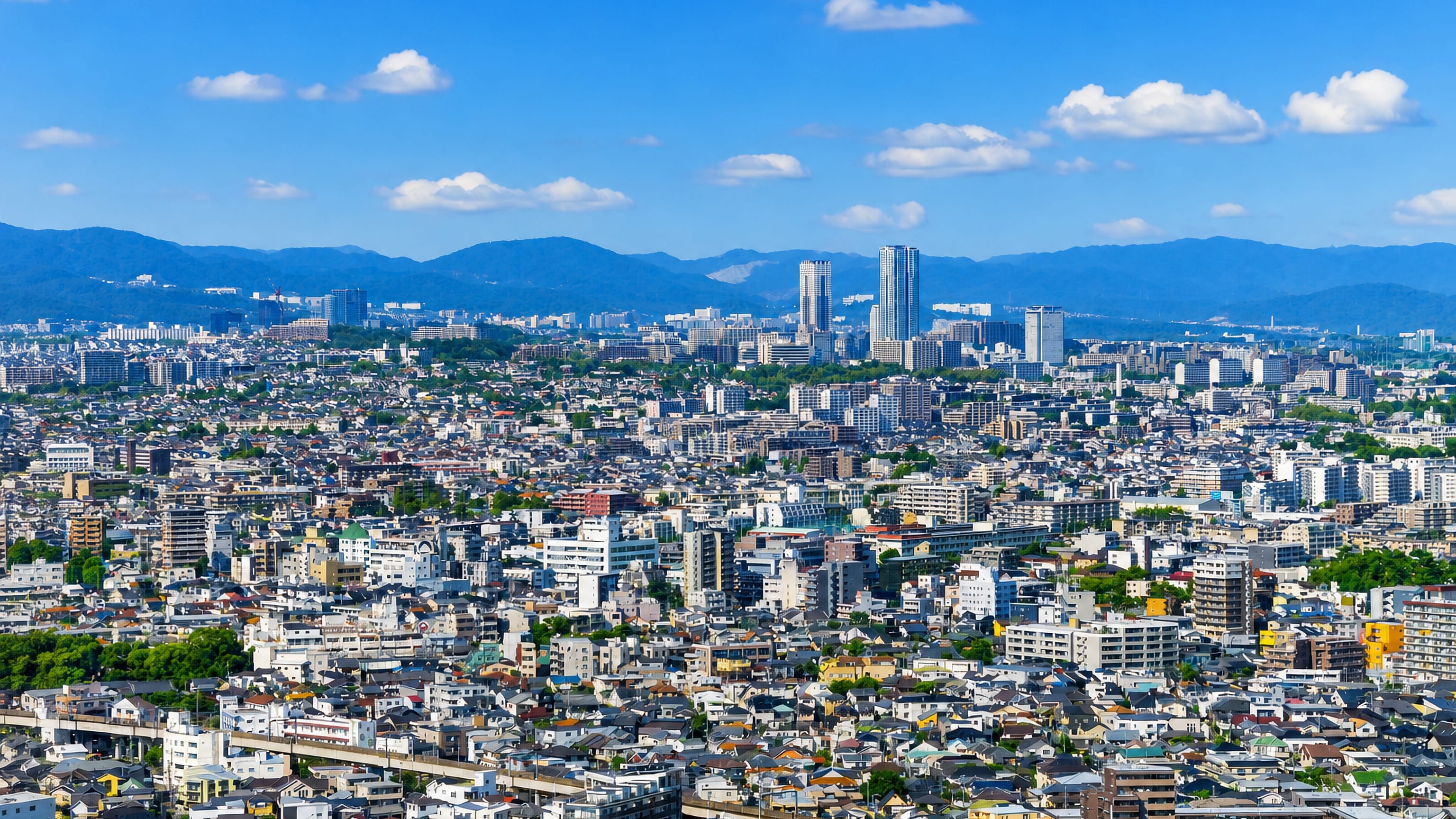 Dense low-rise rooftops of Toyonaka, Japan, with an elevated railway and distant high-rise towers.