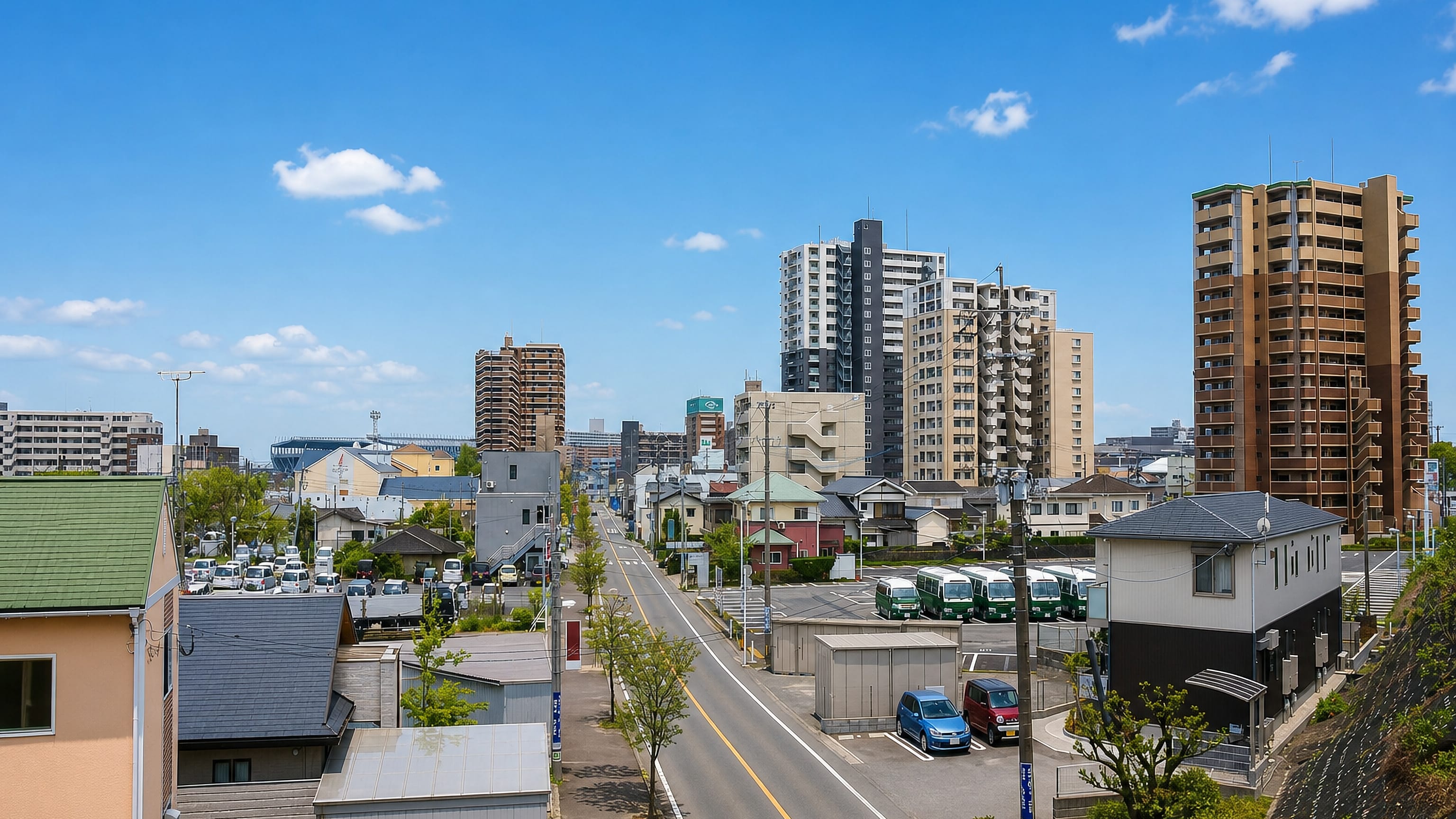Tosu, Saga Prefecture, with low houses and apartment towers lining a straight road under a clear sky.