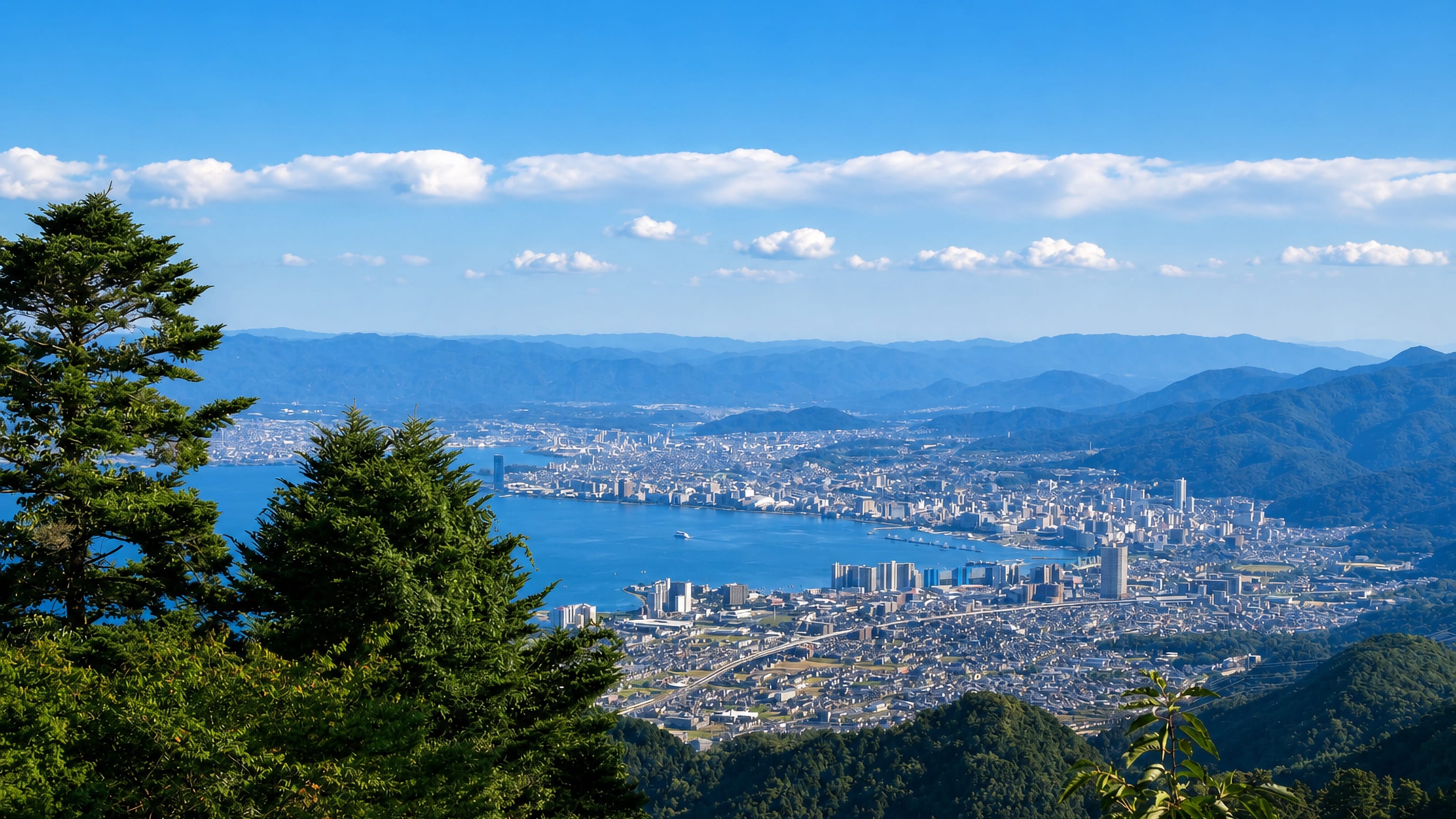 Otsu, Japan, spreading along the shore of Lake Biwa, seen from the forested slopes of Mount Hiei.