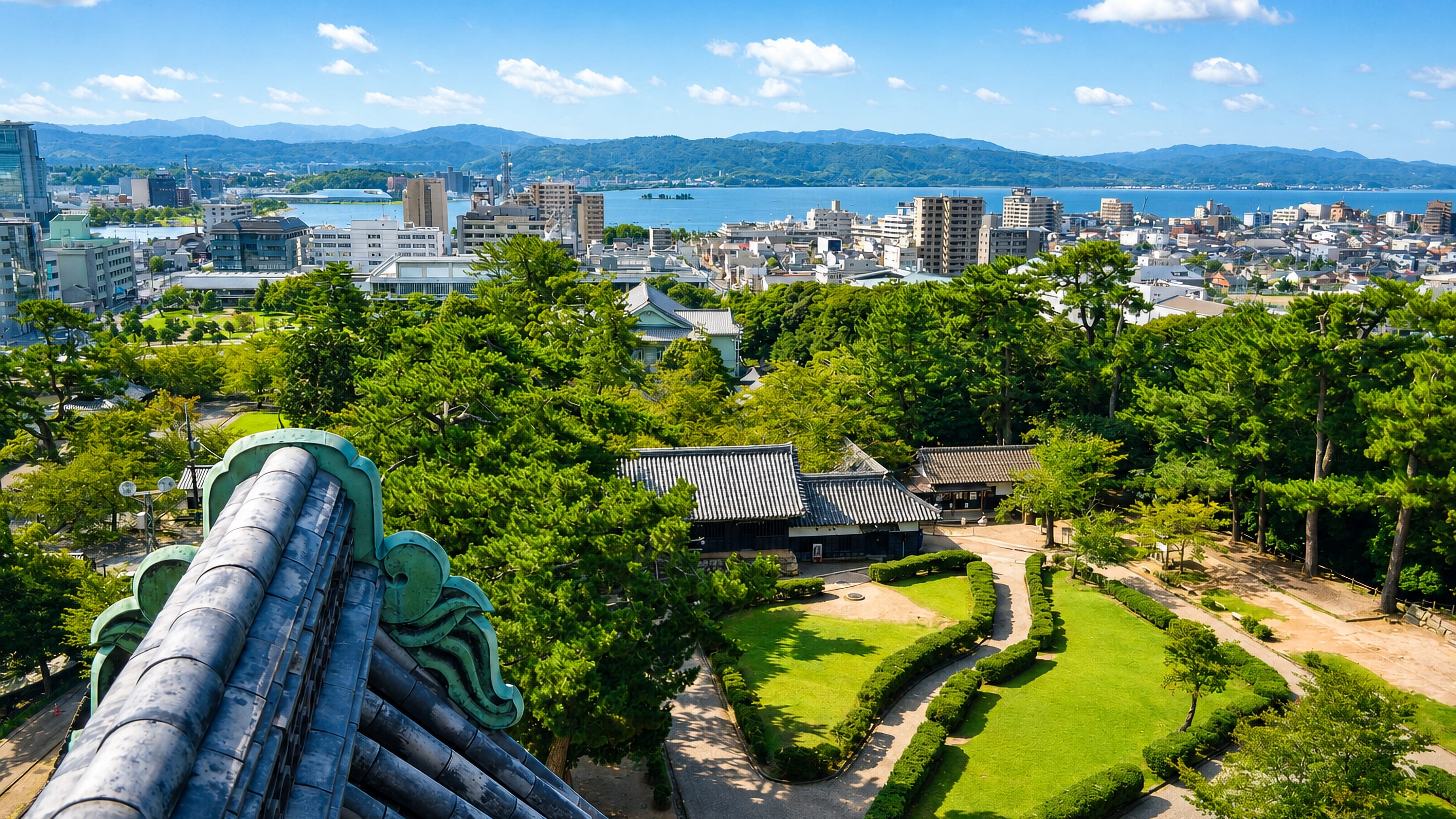 Matsue, Japan, seen from Matsue Castle's tiled roof over pine-filled castle grounds toward Lake Shinji and distant hills.