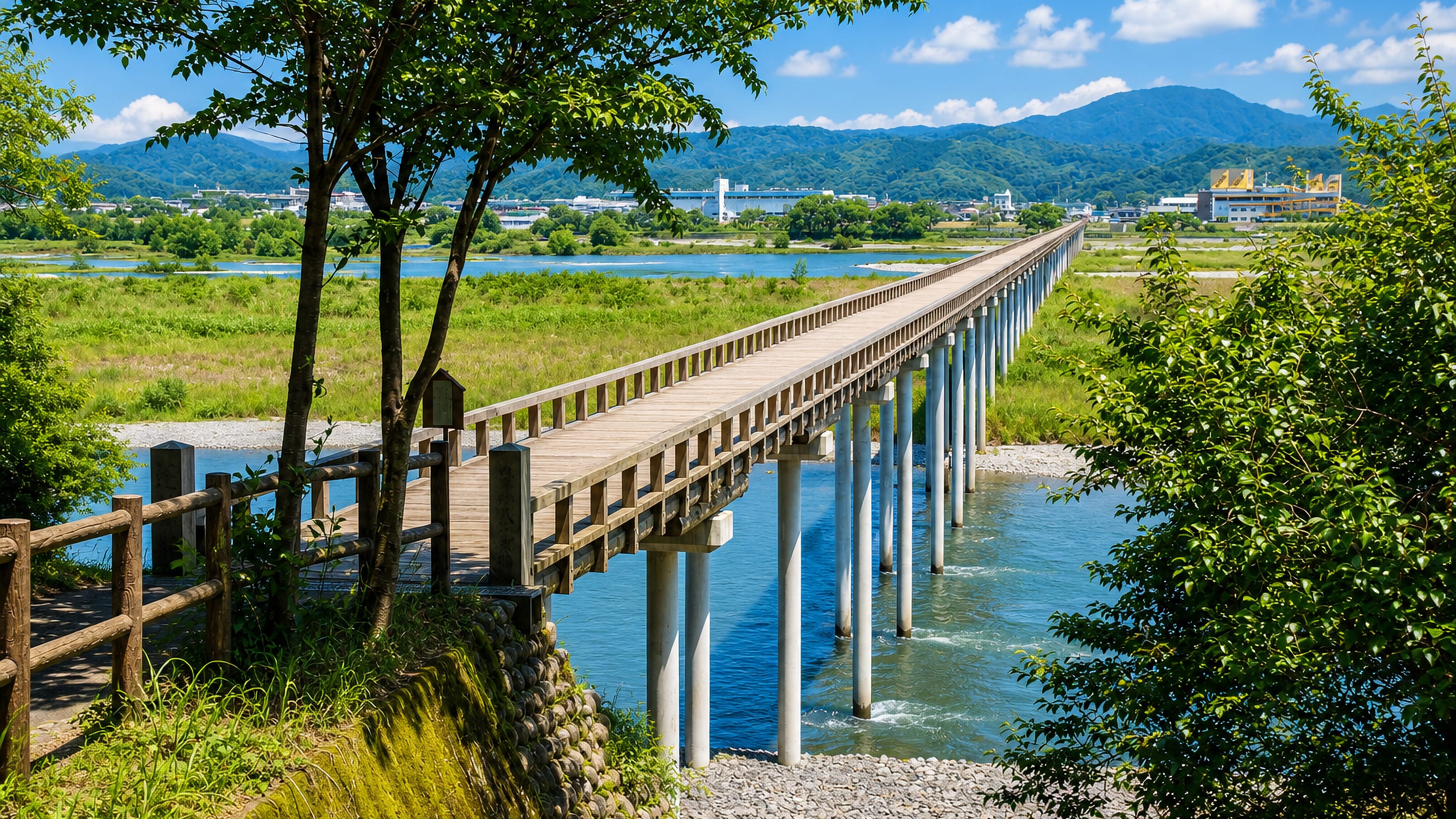 Long wooden footbridge crossing the Ōi River at Shimada, Japan, with the town and mountains beyond.