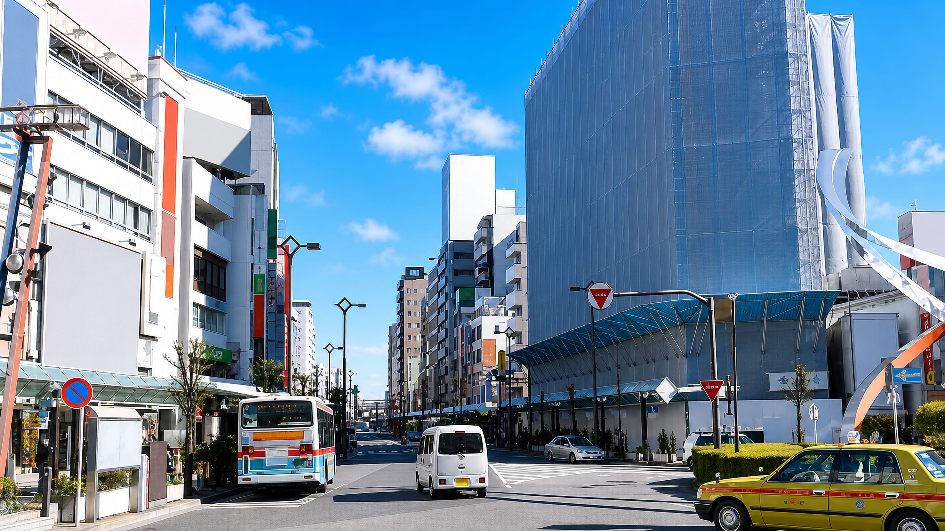Sunny street in Ōta, Tokyo, with a city bus, yellow taxi and mid-rise shops under a wide blue sky.