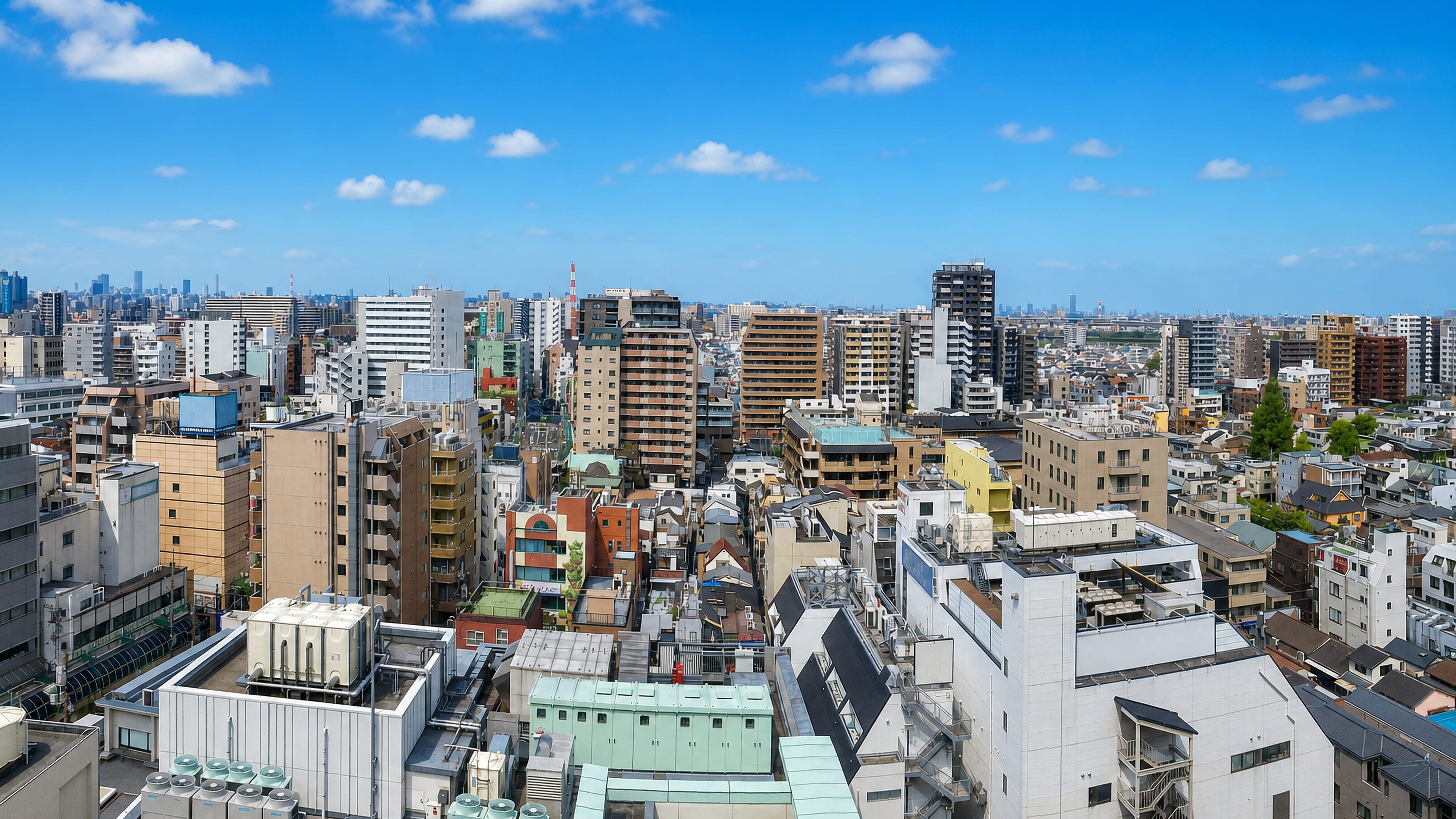 Dense apartment blocks and low-rise rooftops across Adachi, Tokyo, with the city skyline on the horizon
