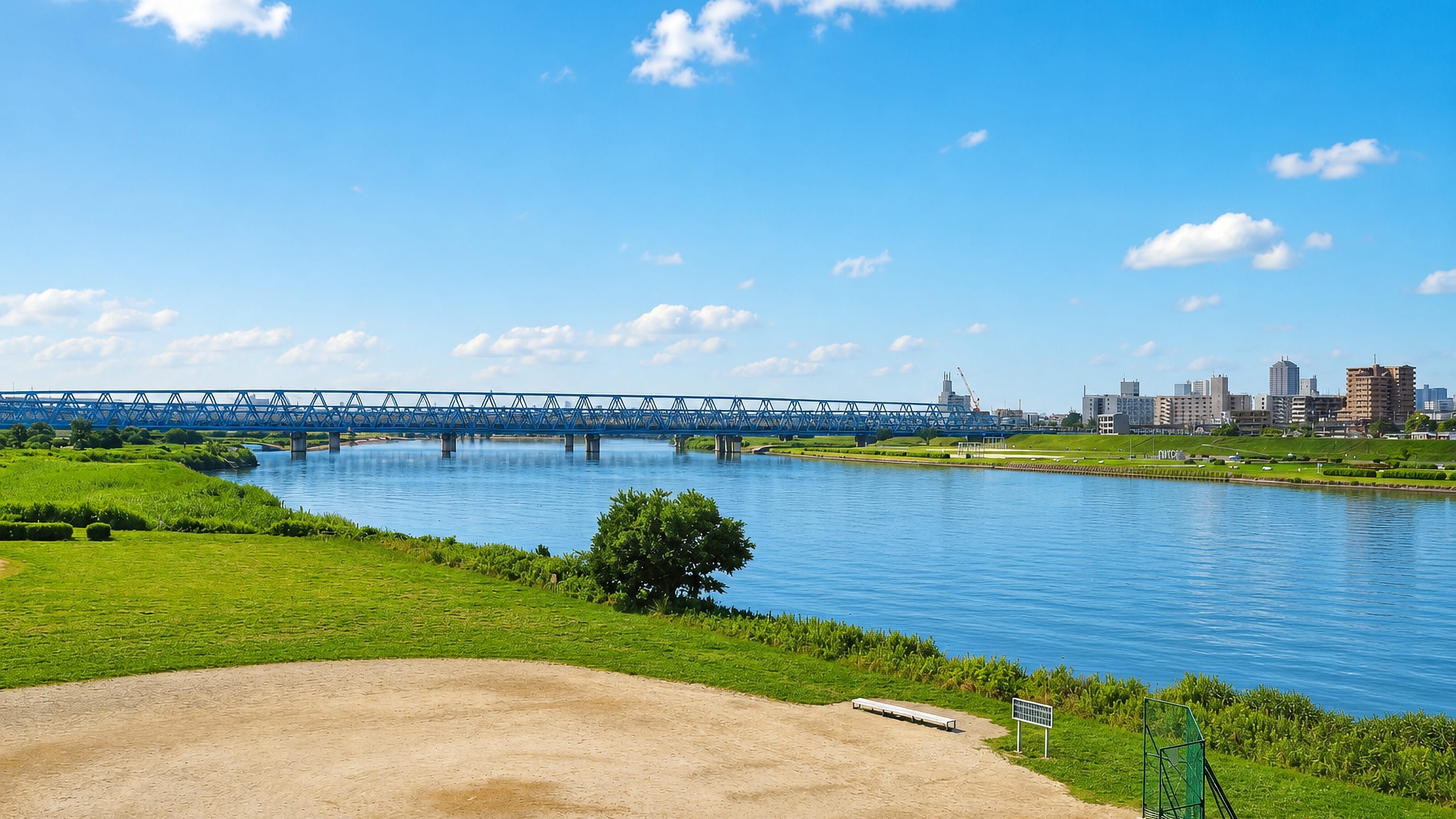 Grassy riverside sports grounds along the Arakawa river with a blue truss railway bridge, Arakawa, Tokyo.