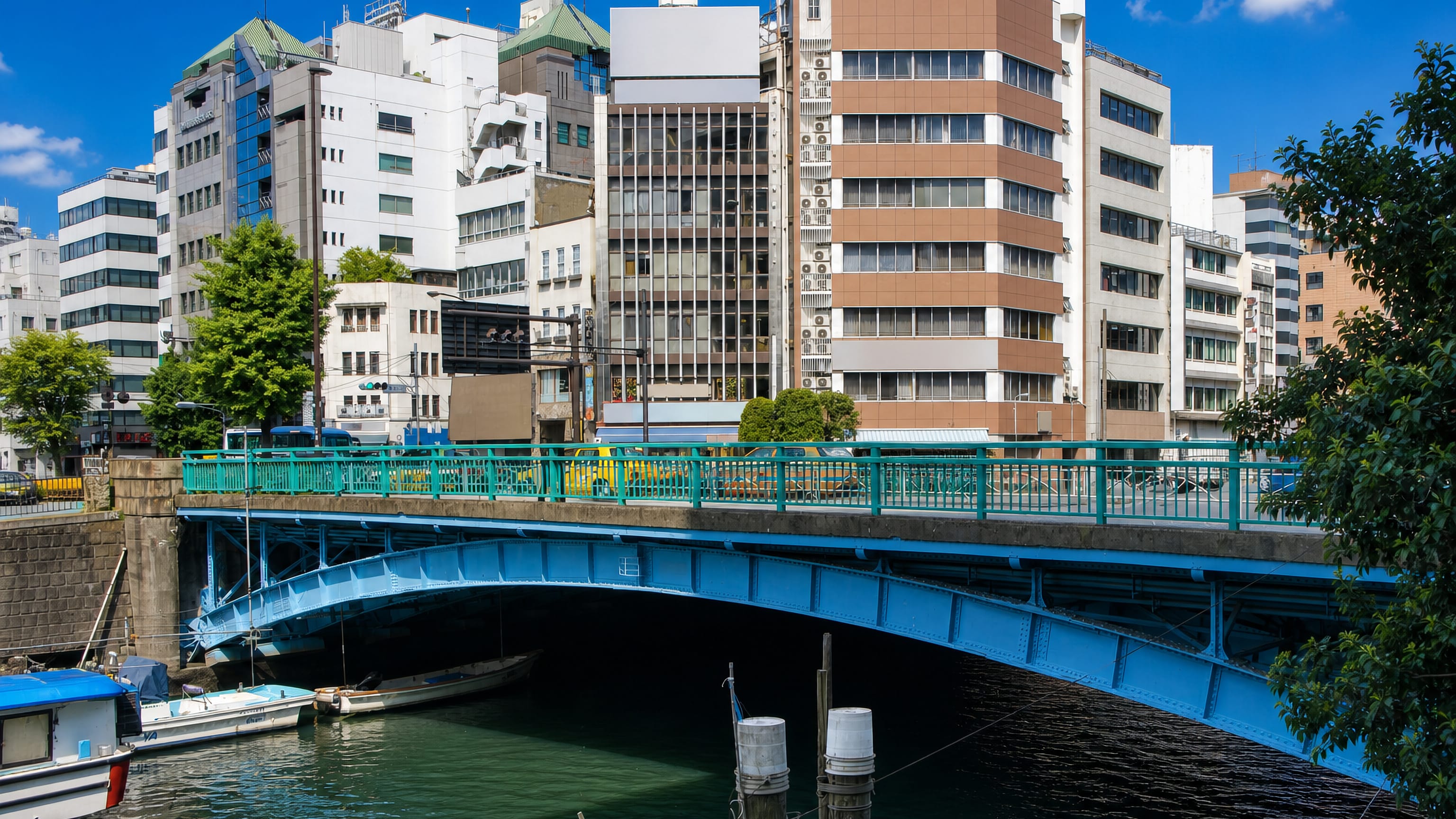 Blue steel arch of the Asakusabashi bridge over Tokyo's Kanda River, with moored boats and riverside offices.