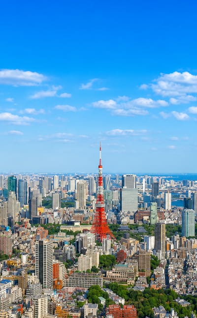 Tokyo skyline with the red-and-white Tokyo Tower and distant Tokyo Skytree above dense districts and the bay.