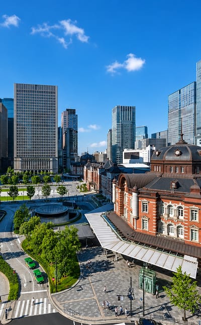 Tokyo Station's red-brick Marunouchi building backed by the Chiyoda skyscraper cluster under blue sky.