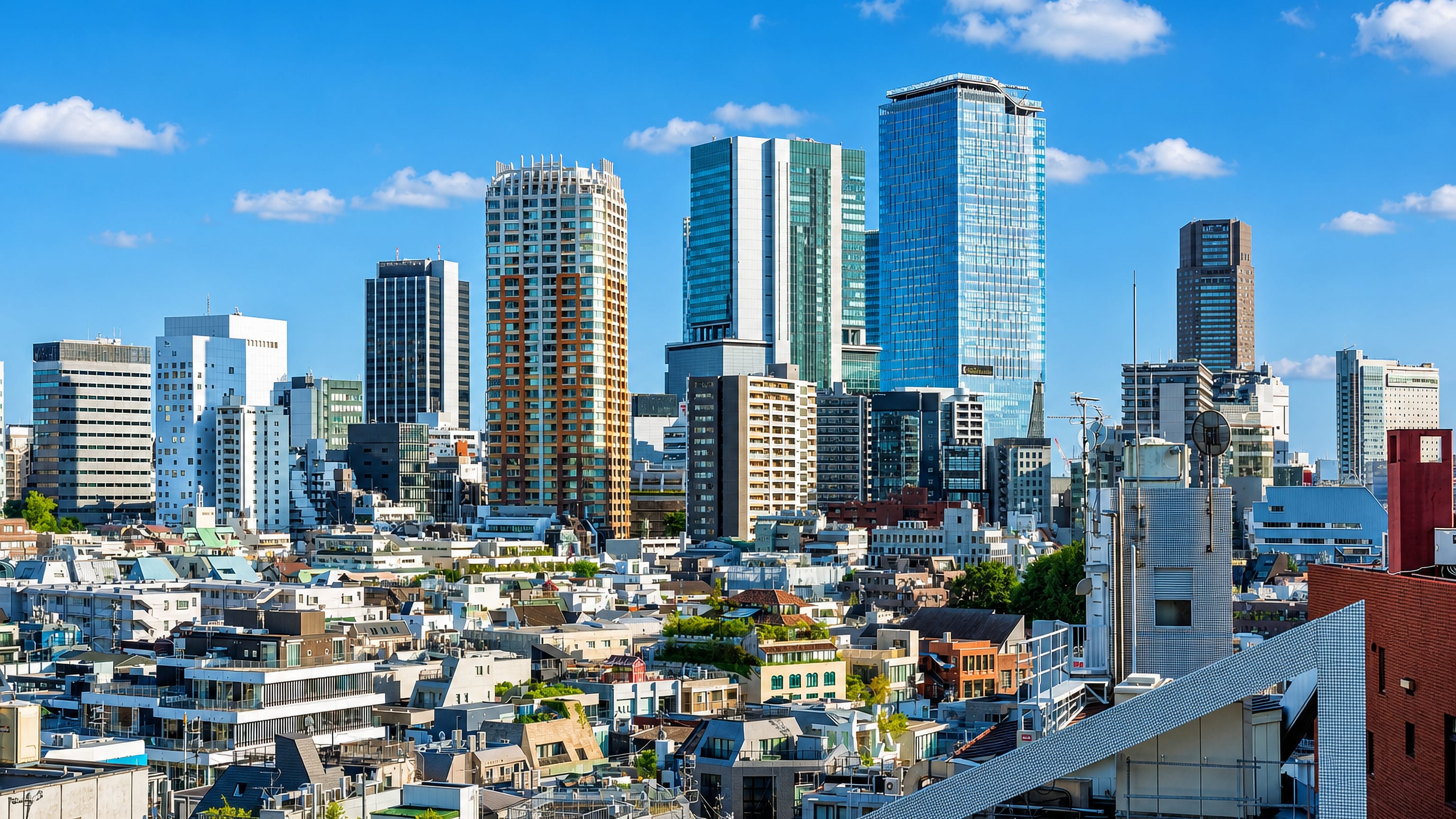 Shibuya rooftops in Tokyo backed by a cluster of glass and concrete high-rise towers under a clear sky
