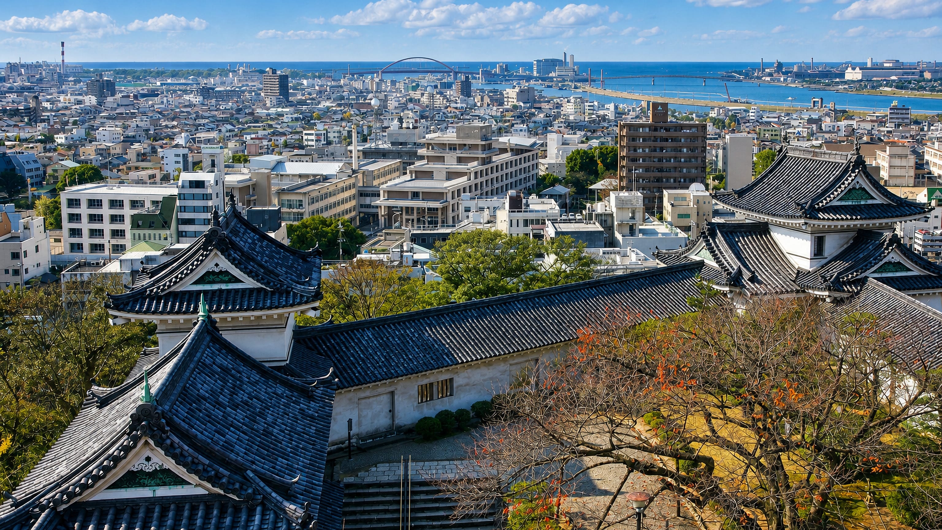 Wakayama Castle rooftops above the city, with the Kinokawa river mouth, port and Kii Channel beyond