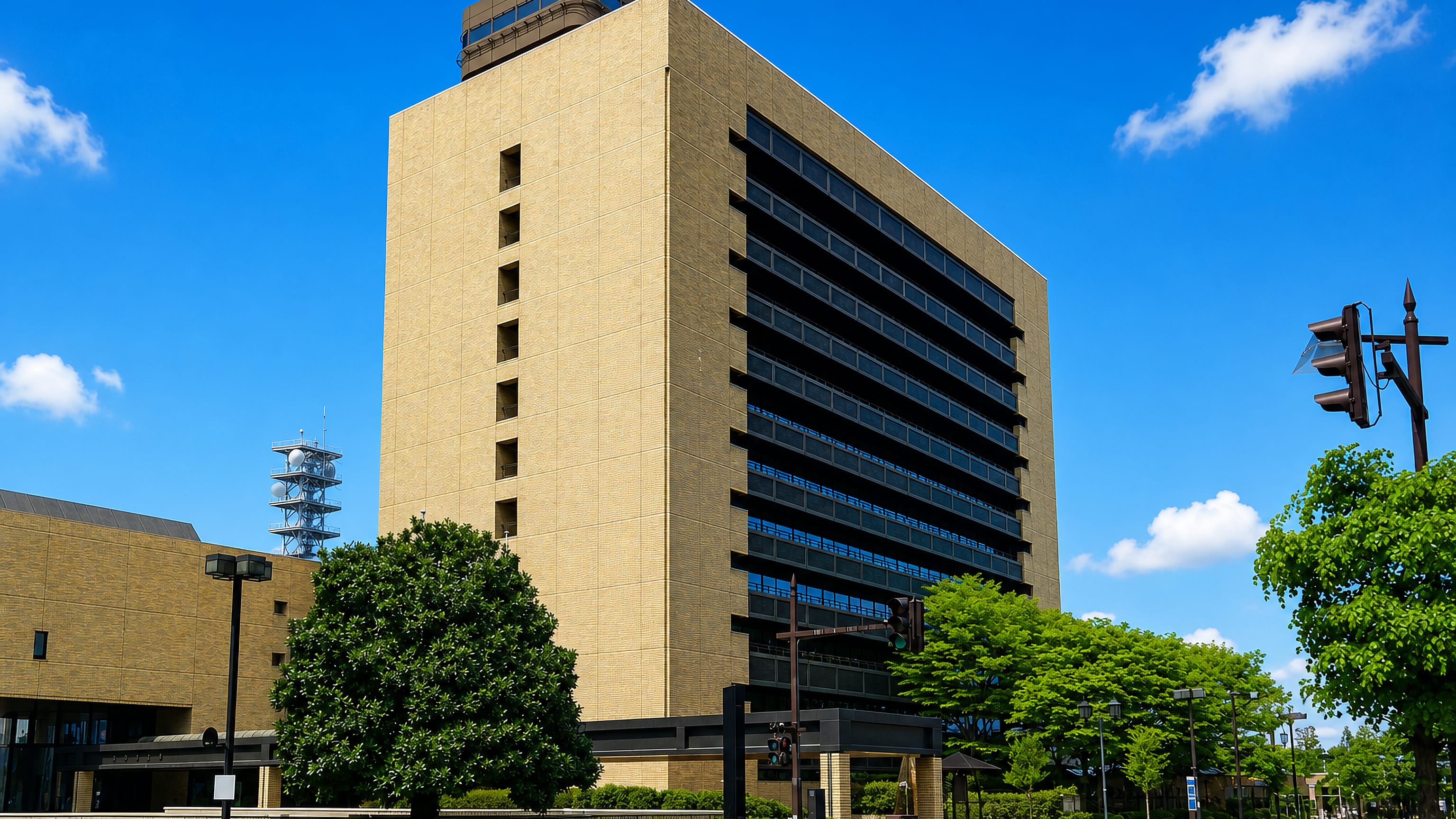Tan modernist government high-rise on a broad tree-lined avenue in Yamagata, Japan, under clear blue sky.