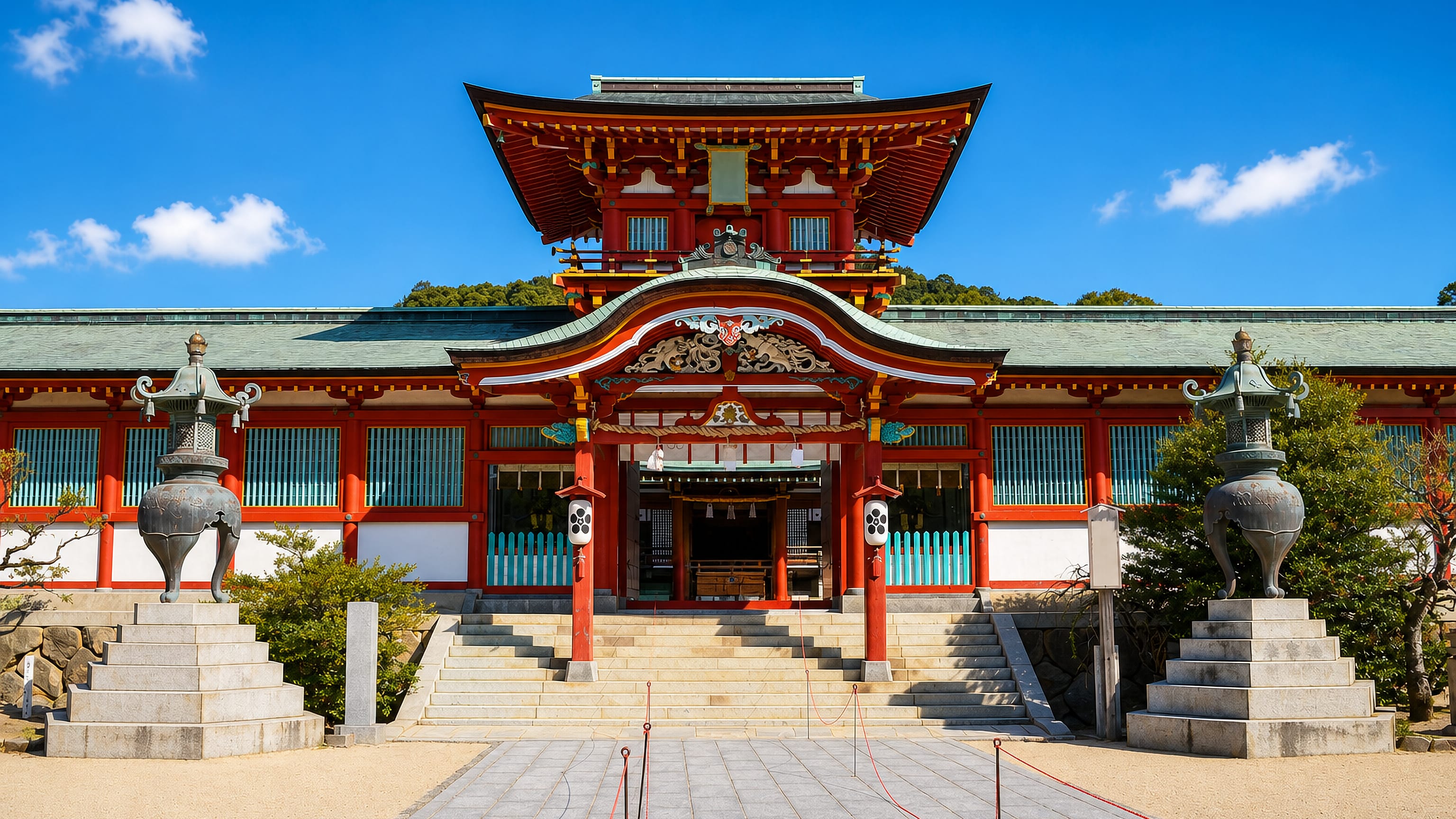 The red-and-green main hall of Hofu Tenmangu shrine in Hofu, Japan, seen across its stone forecourt.