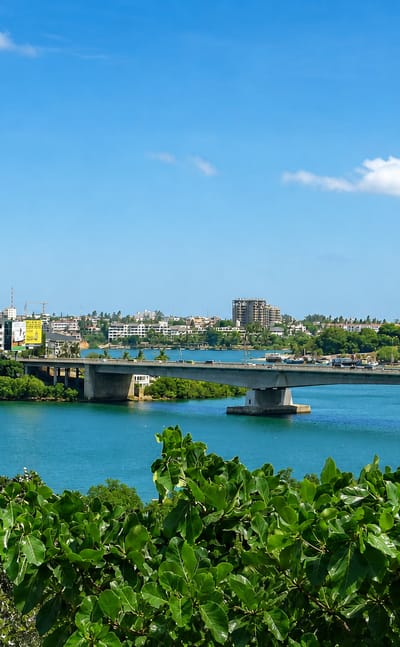 Nyali Bridge spanning Tudor Creek with Mombasa's skyline beyond lush green foreground foliage