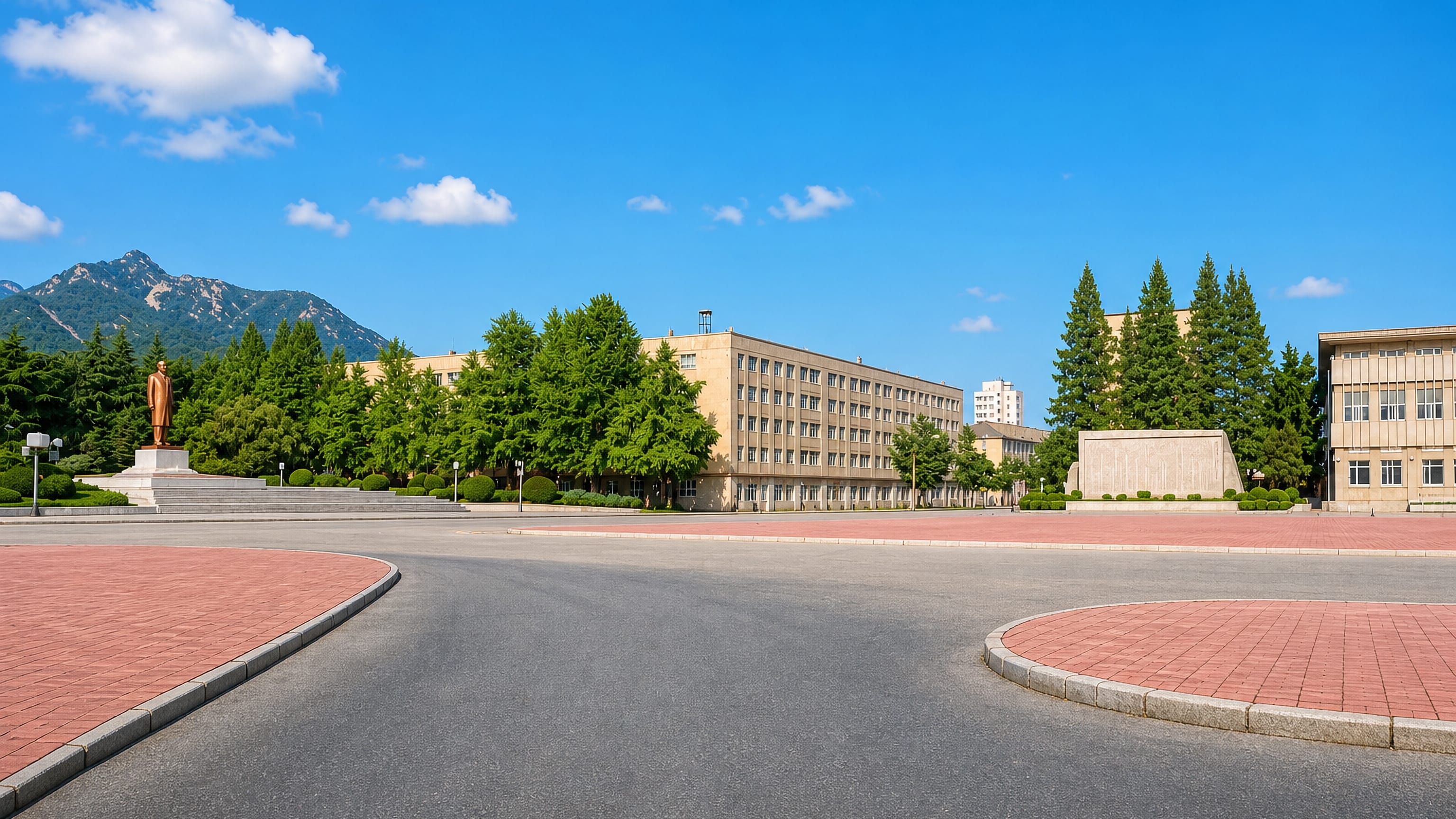 Broad civic square with a bronze statue and a government building below wooded hills in Haeju, North Korea.