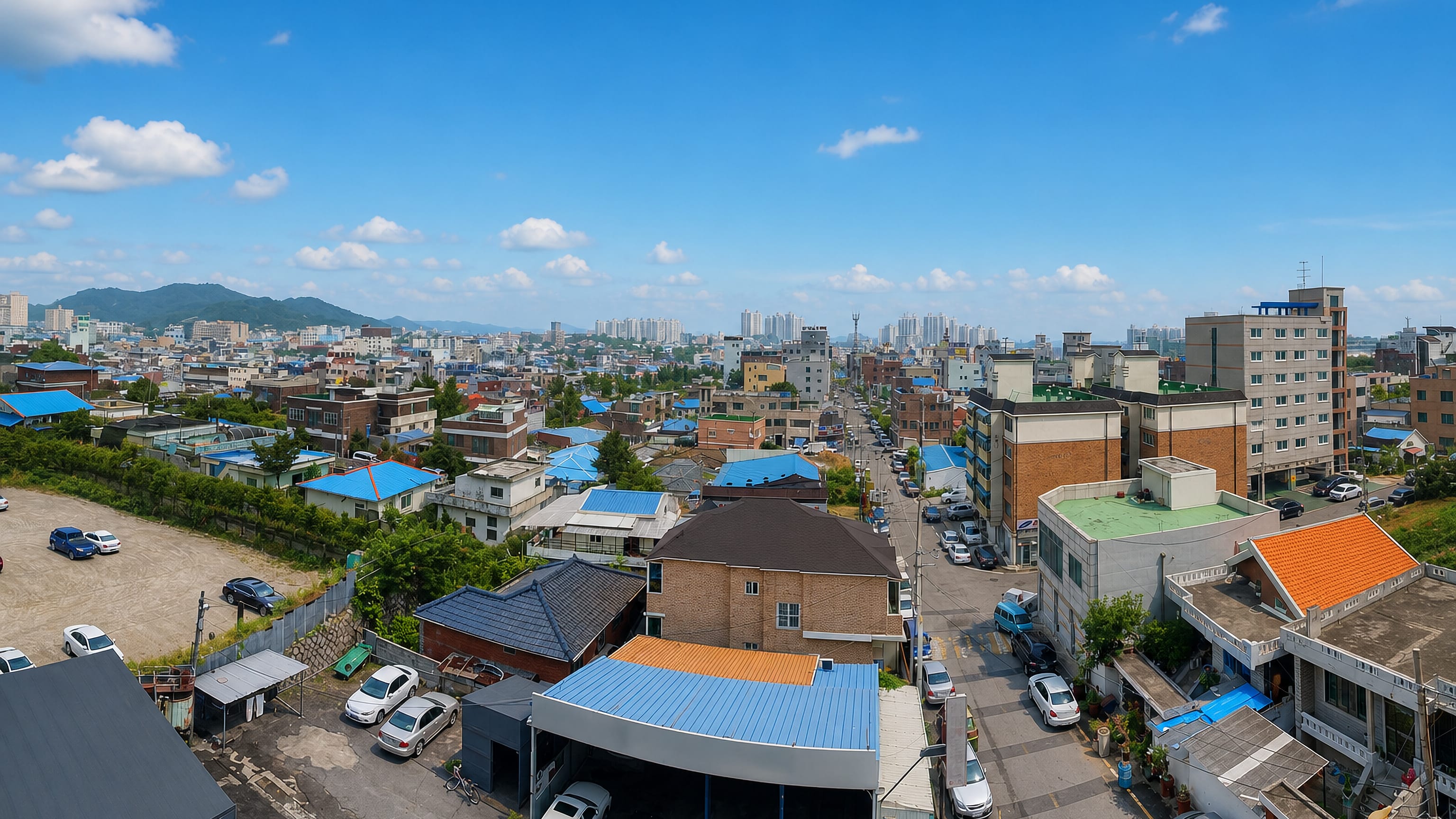 Asan, South Korea, from above: blue-roofed low-rise streets in the foreground with distant apartment towers.