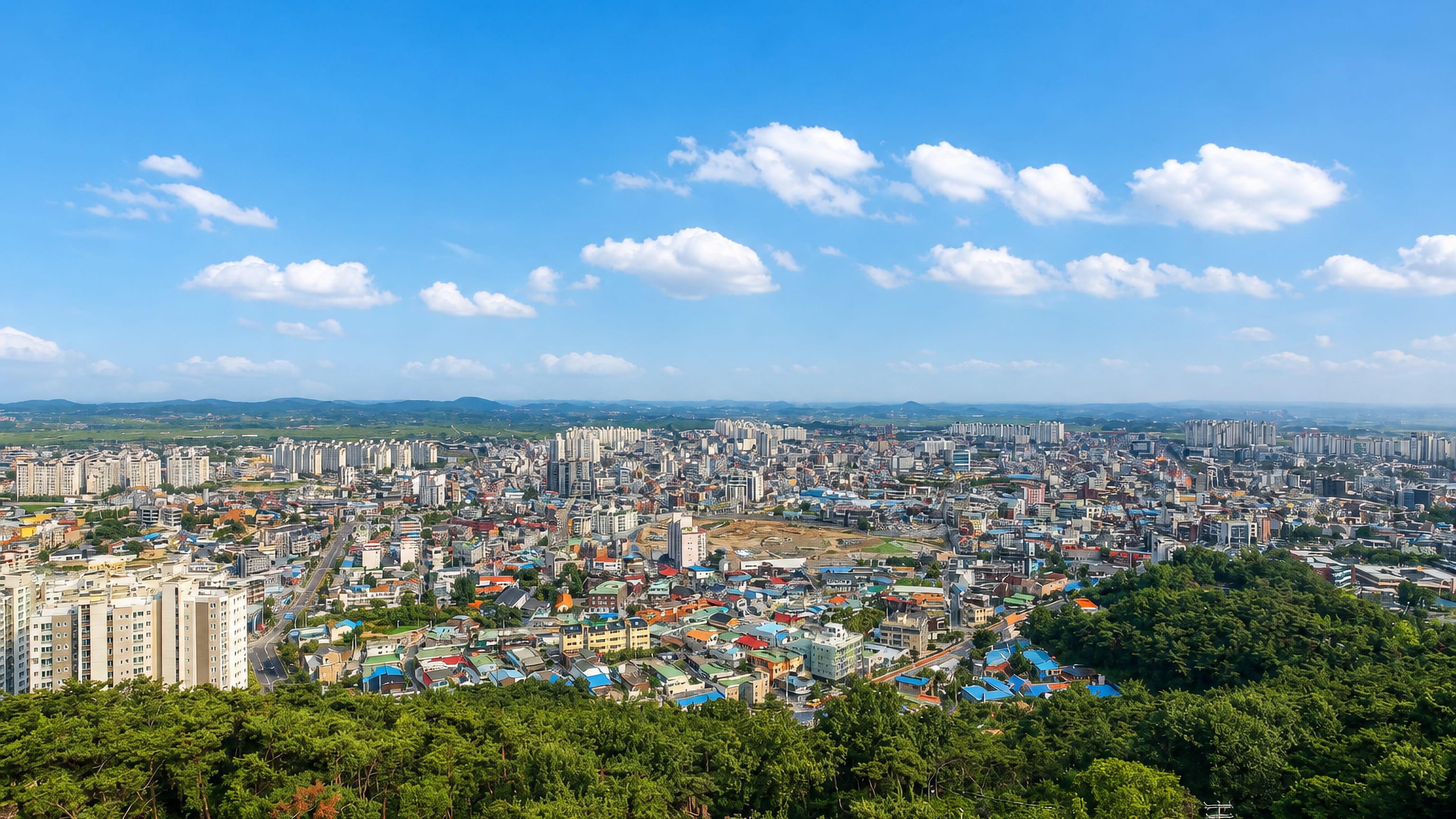 Seosan, South Korea, seen from a wooded hilltop, with apartment blocks and low hills stretching to the horizon.