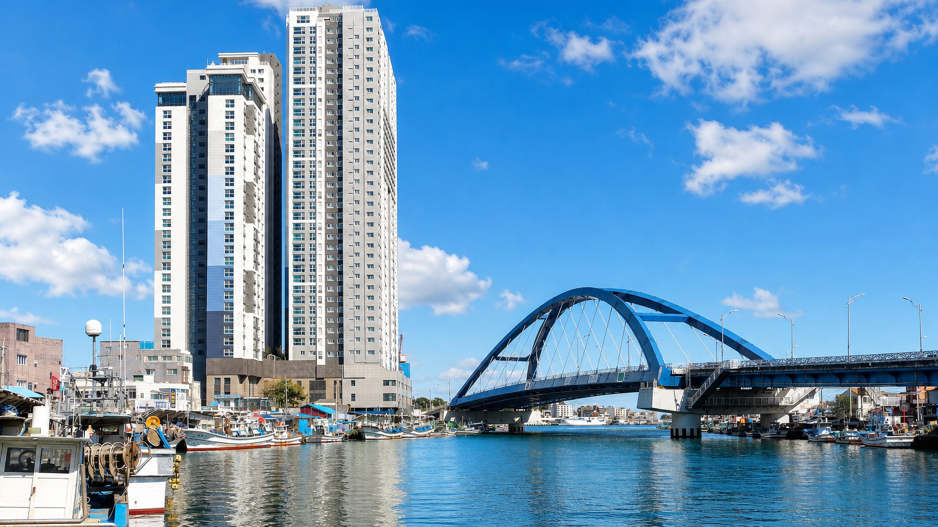 Fishing boats and high-rise apartments beside the blue arch bridge spanning Sokcho's harbour channel.