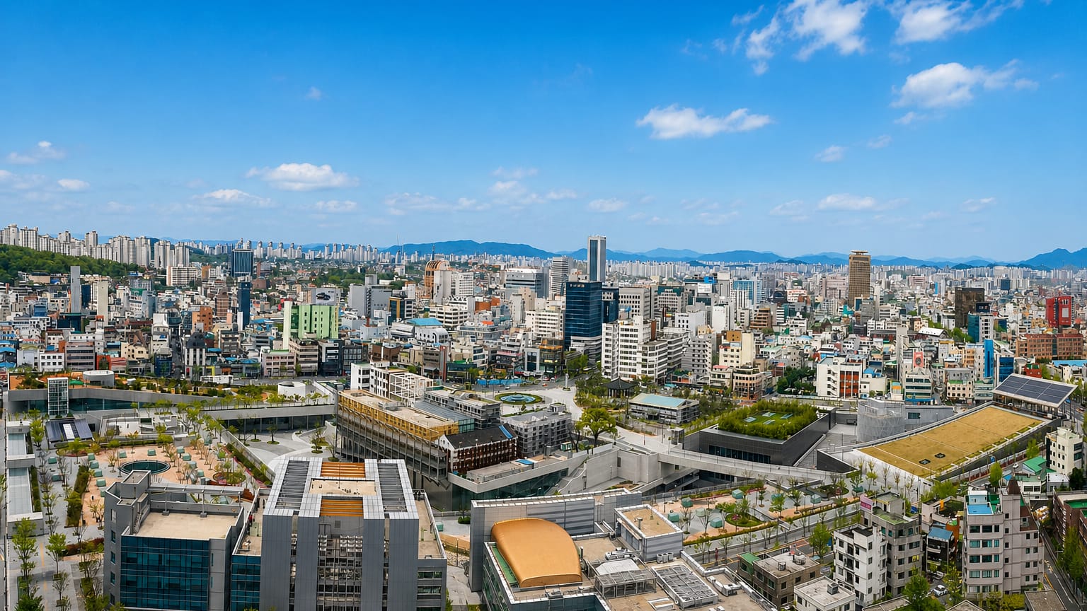 Wide view over downtown Gwangju and a low cultural-plaza complex with distant mountains, South Korea.