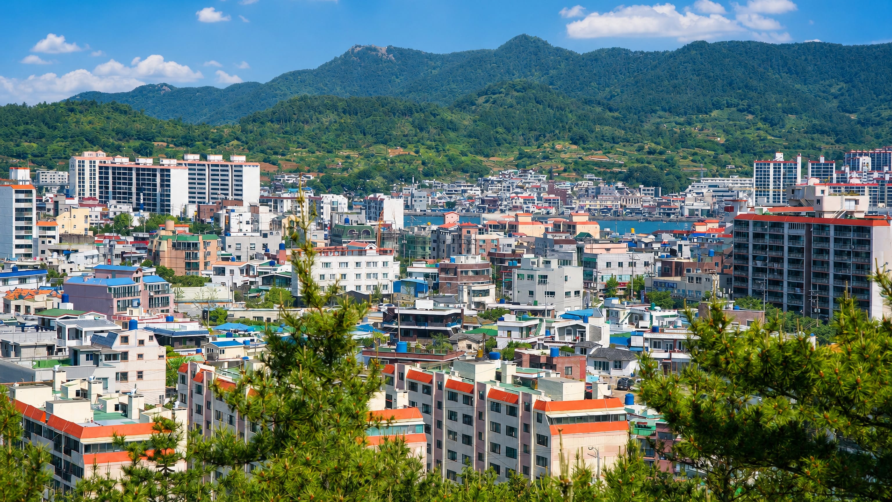 Colourful hillside housing and the harbour of Tongyeong, South Korea, ringed by green mountains.