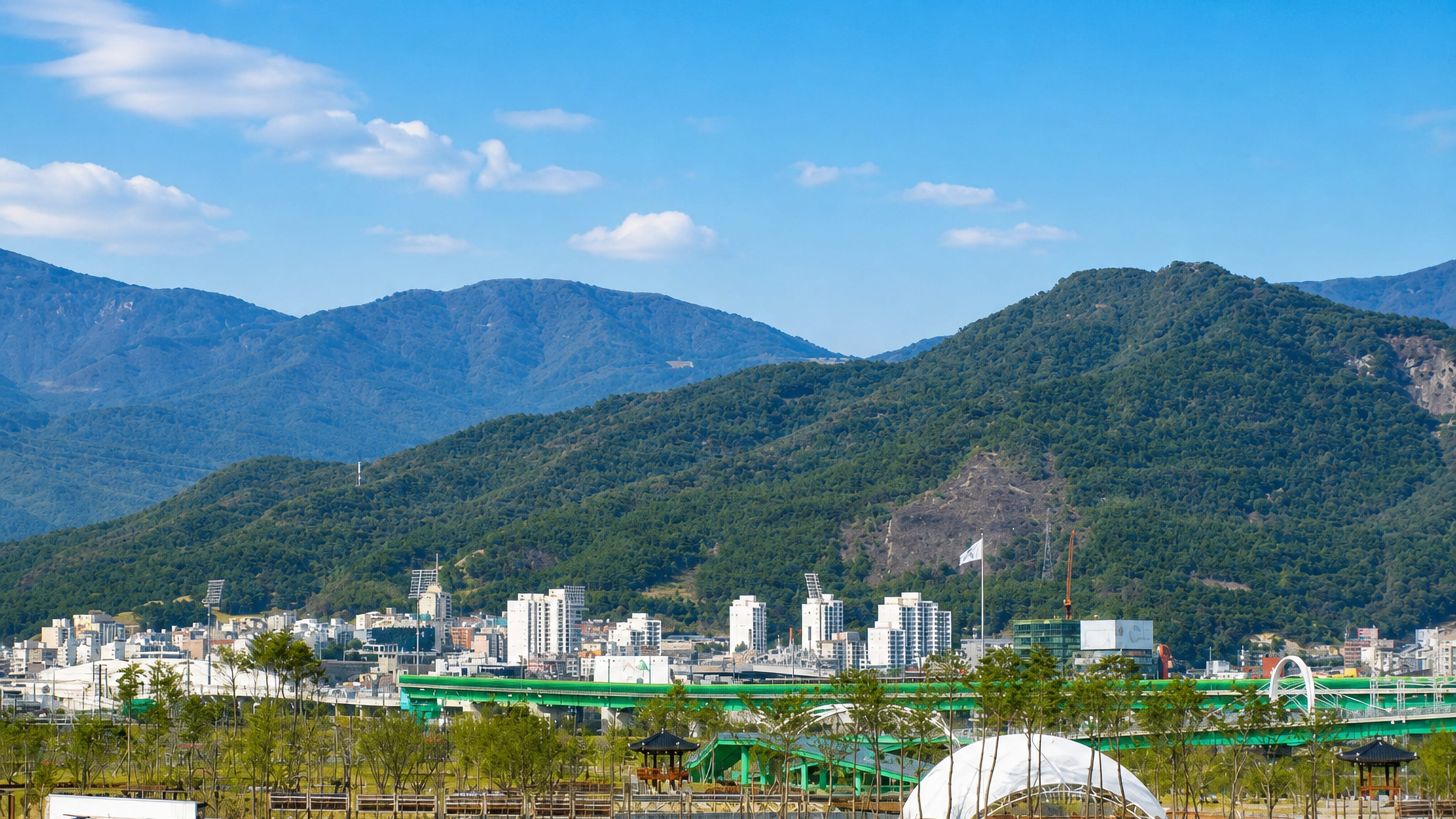 Yangsan's apartment blocks and a green elevated expressway below the forested mountains of Gyeongsangnam-do.