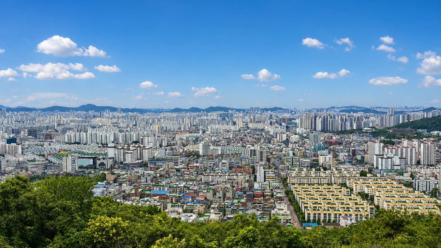 Dense apartment blocks of Incheon stretching across the plain below a forested hill in South Korea.