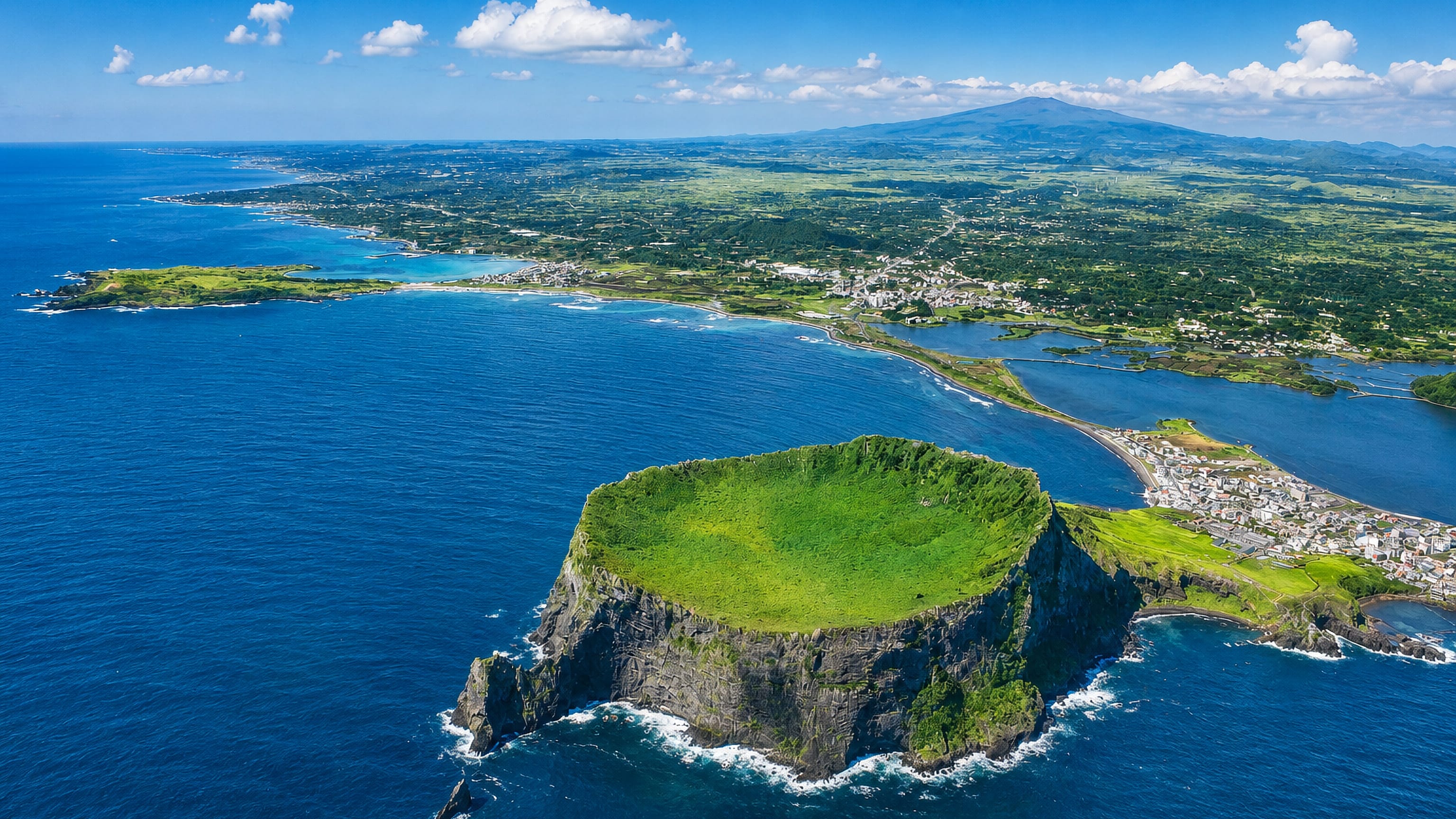 Seongsan Ilchulbong tuff cone rising from the sea off Seogwipo, Jeju, with Hallasan in the distance.