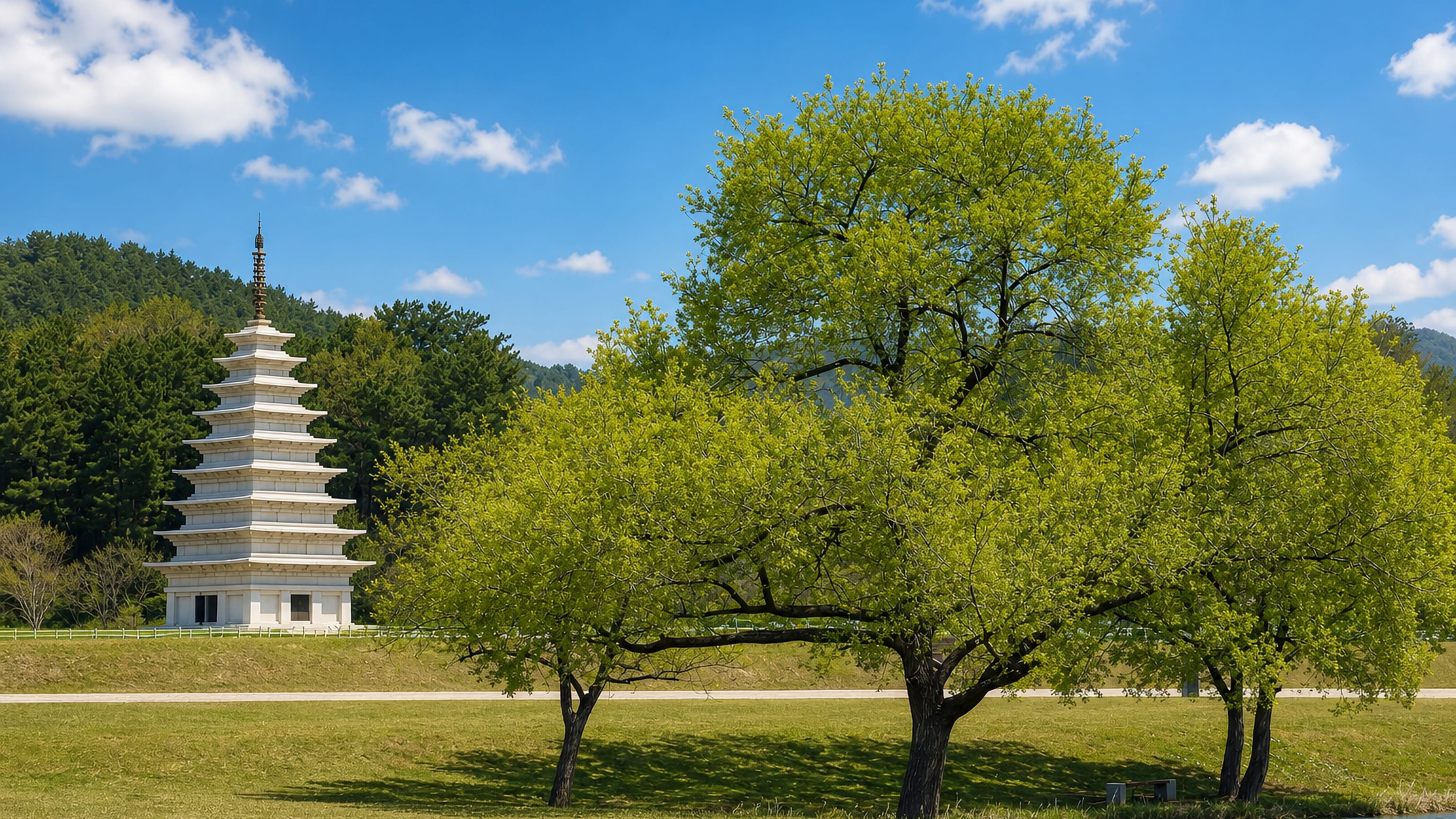A tall white stone pagoda standing in open parkland below wooded hills in Iksan, South Korea.