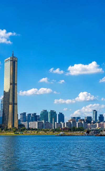 Seoul's Yeouido skyline along the Han River, anchored by the golden 63 Building tower under a blue sky.