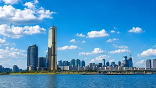 Seoul's Yeouido skyline along the Han River, anchored by the golden 63 Building tower under a blue sky.