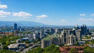 Almaty cityscape with green-roofed towers and buildings set against the Tian Shan mountains, Kazakhstan.