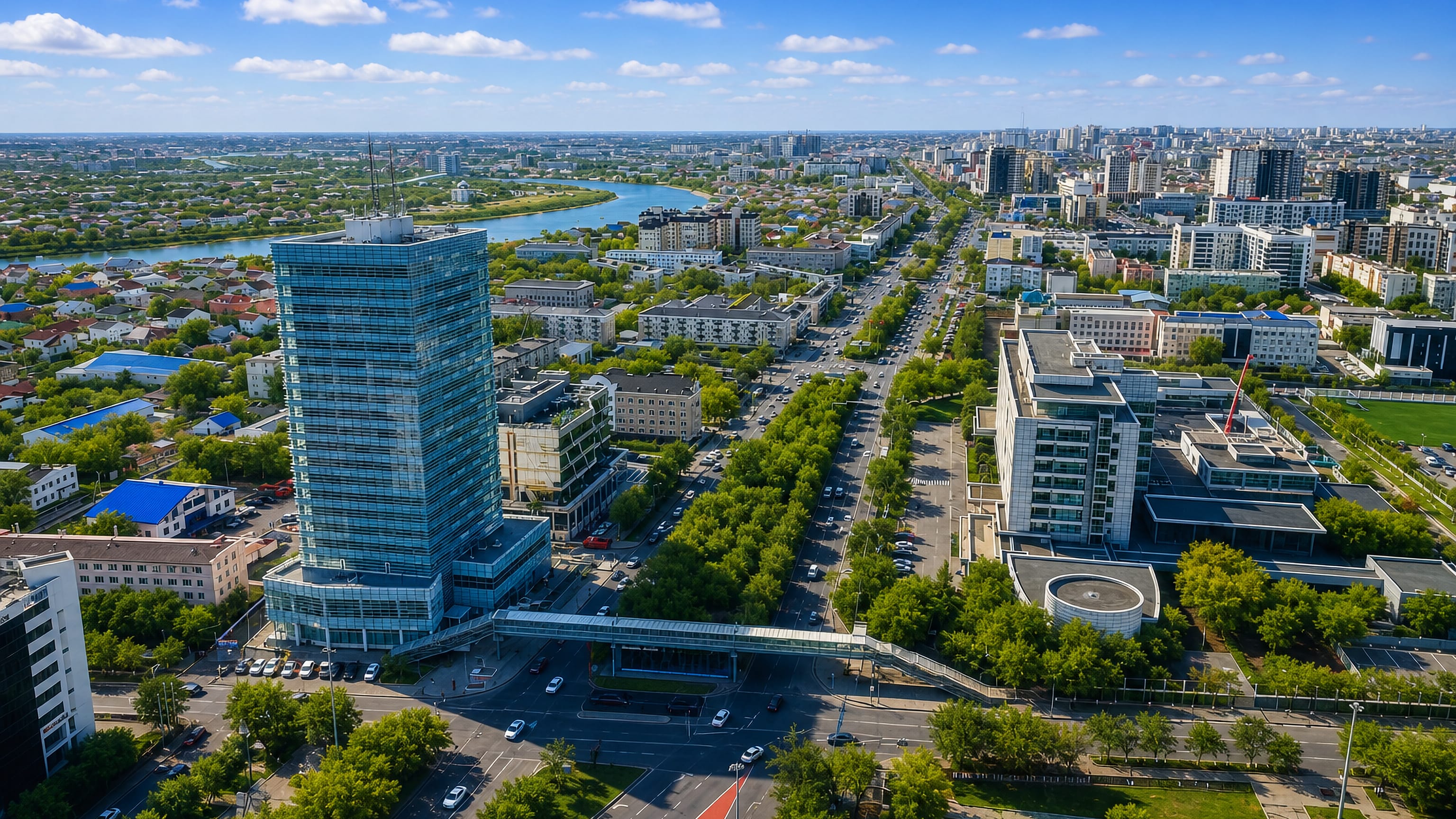 Aerial view of Atyrau, Kazakhstan, with a blue glass tower, tree-lined boulevards and a river beyond.