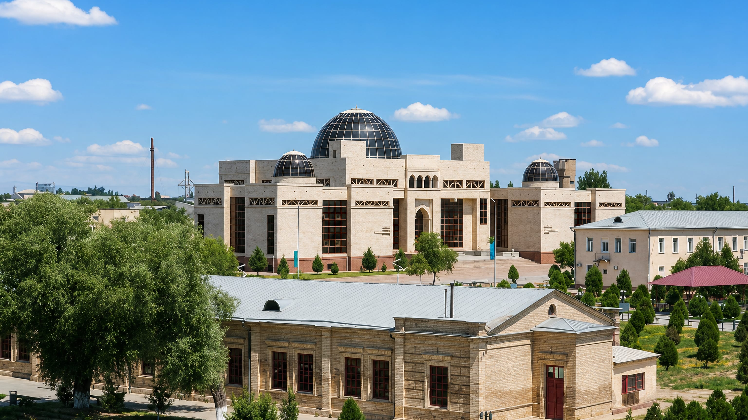 Modern stone museum with dark glass domes and an older brick hall among trees in Turkistan, Kazakhstan.