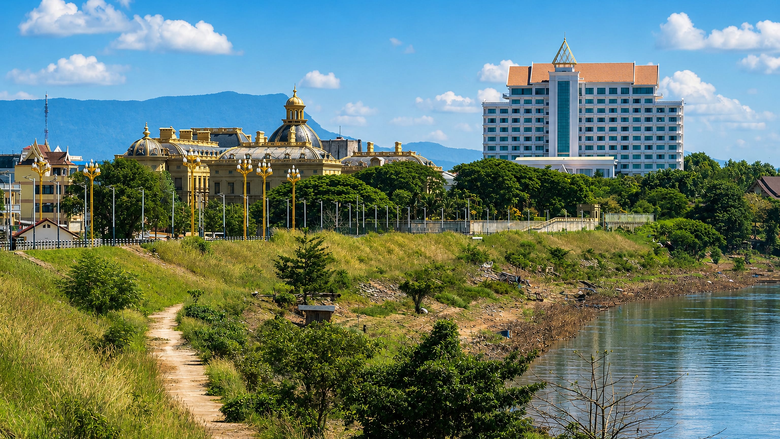 Mekong riverbank at Pakse, Laos, with a gold-domed landmark and a large hotel tower against forested hills.